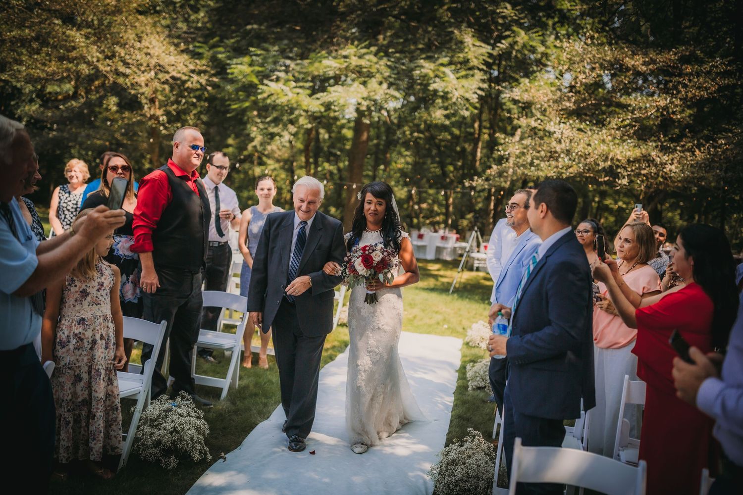 Intimate outdoor wedding ceremony taking place along a decorated garden walkway.
