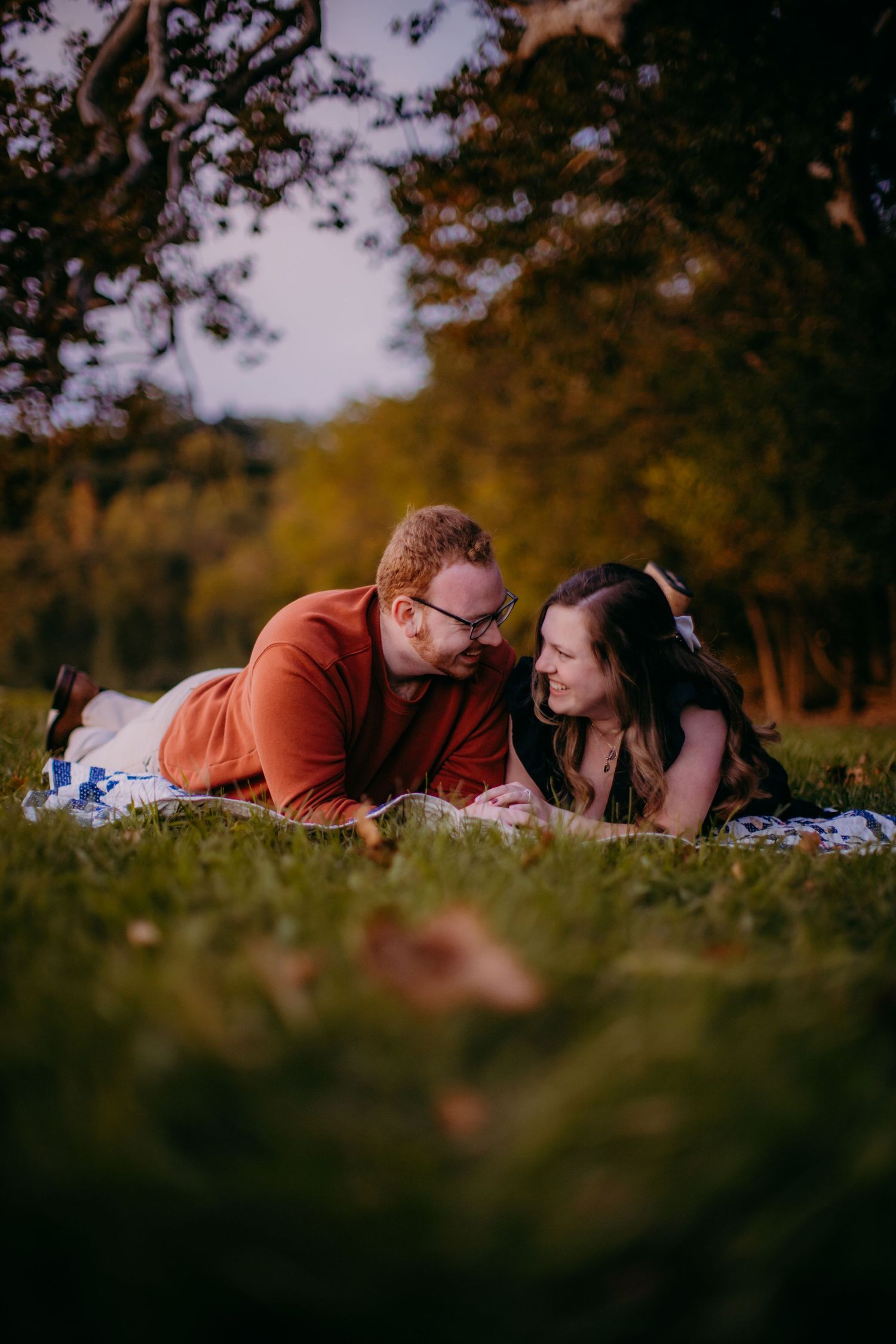 Intimate outdoor photo shoot of couple on blanket surrounded by autumn trees.
