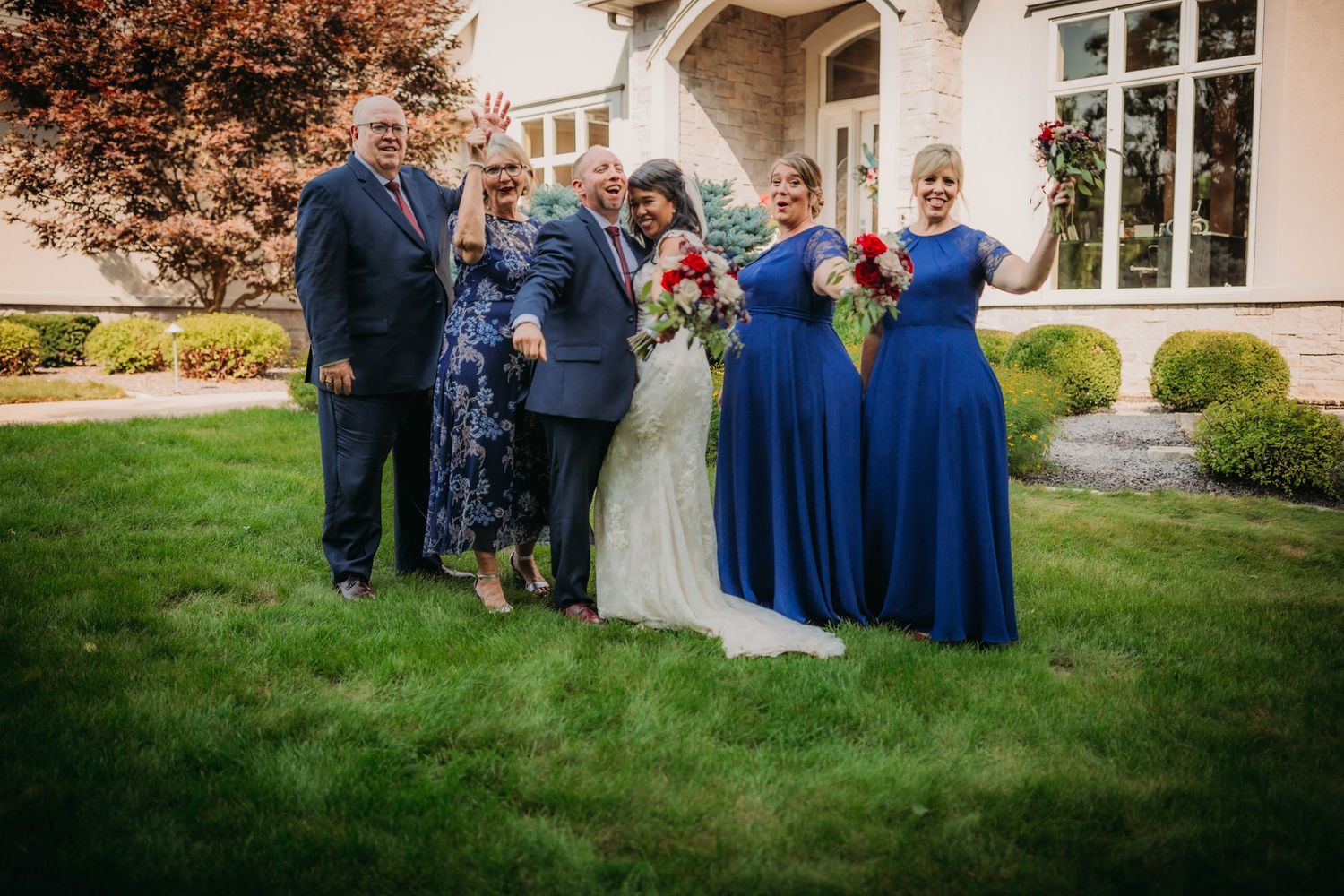 Wedding group photo session with bridesmaids in blue dresses outside an elegant venue.