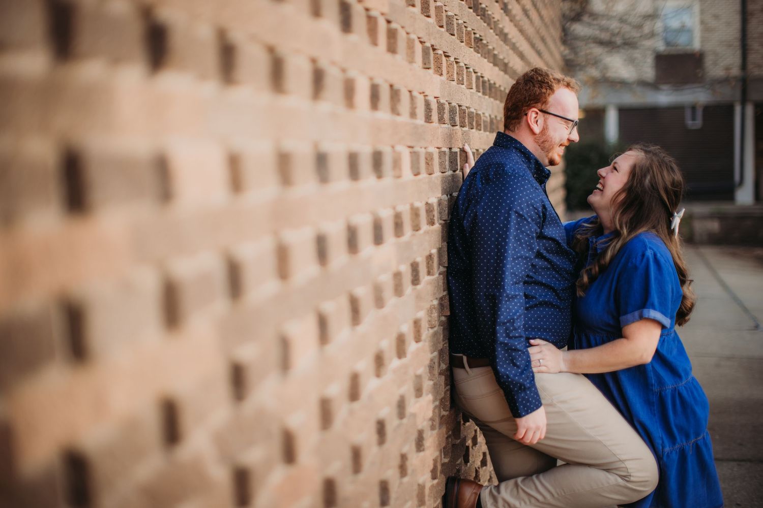 An intimate portrait of a couple sharing a romantic moment against a patterned brick wall.