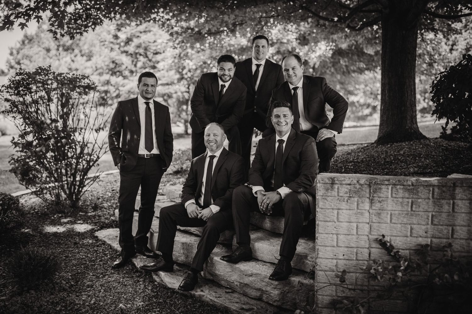 Black and white portrait of groomsmen arranged on stone garden steps.