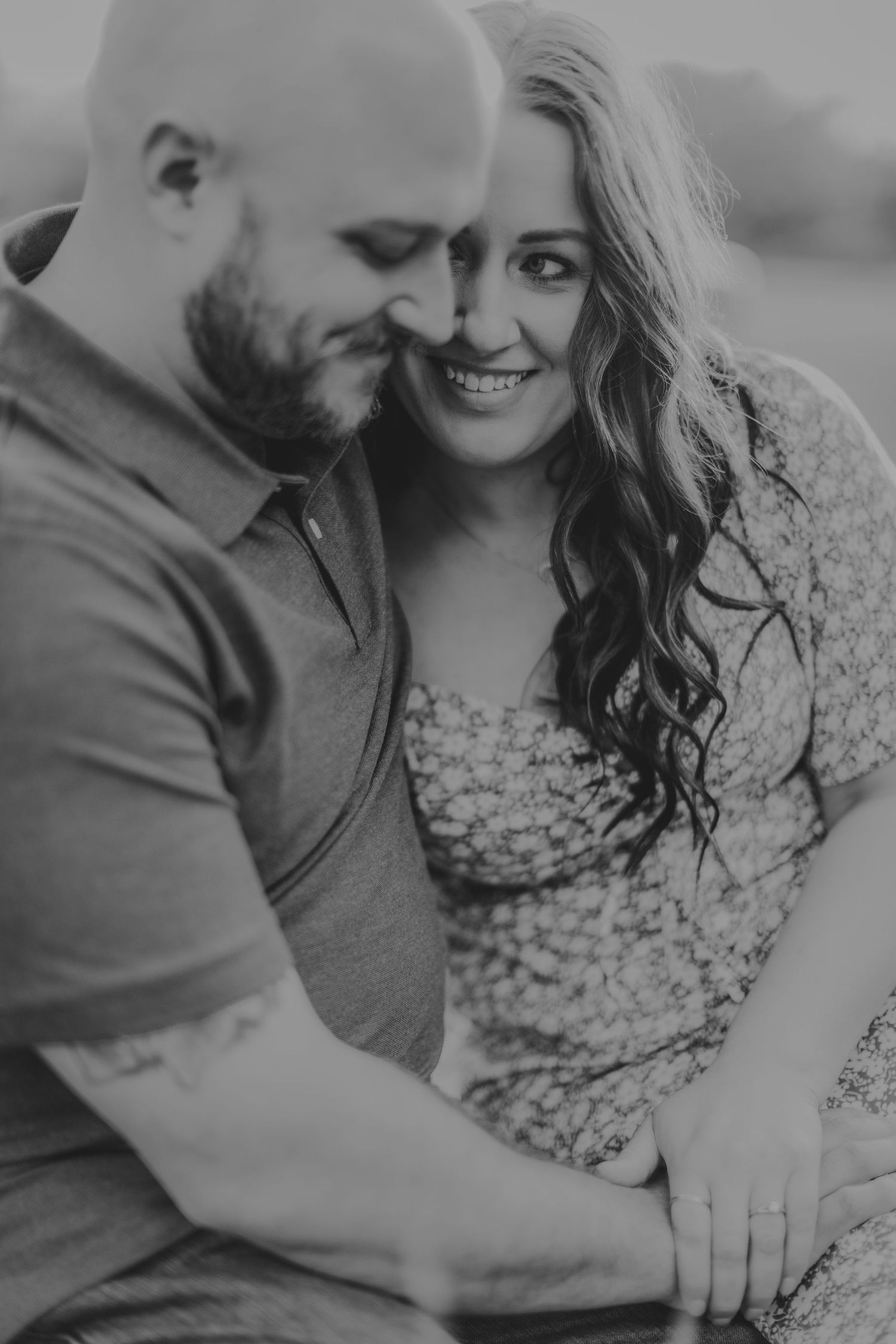 A black and white engagement photo showing a couple sharing a joyful, intimate moment outdoors.