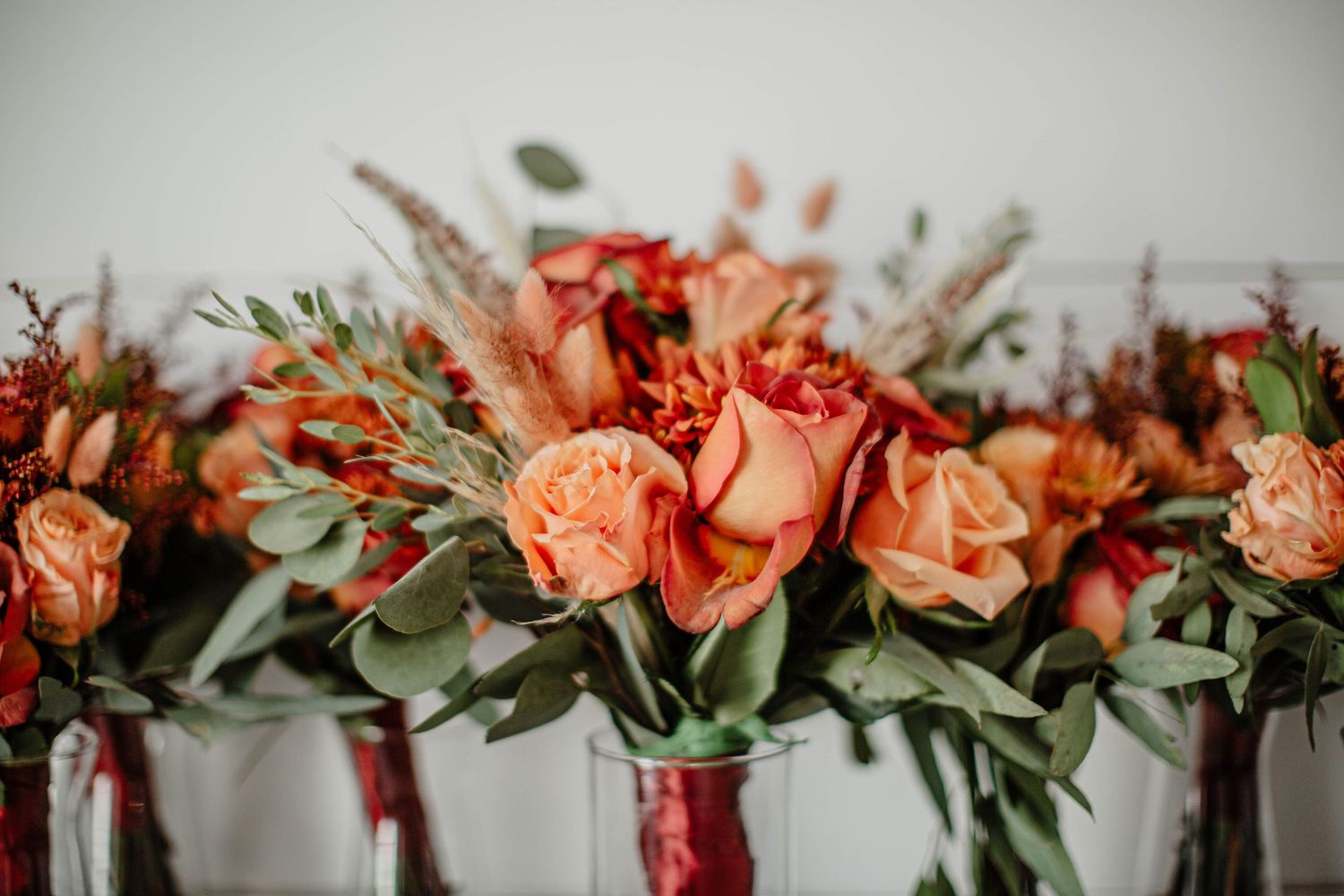 Close-up of coral roses and eucalyptus arranged in metallic vases.