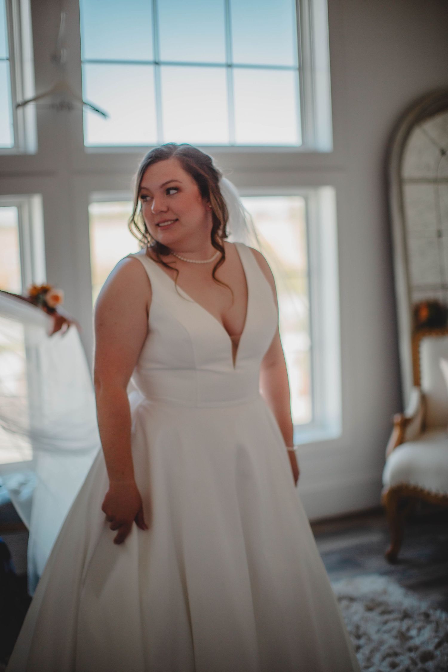 A radiant bride poses in a plunging v-neck wedding dress near bright windows.
