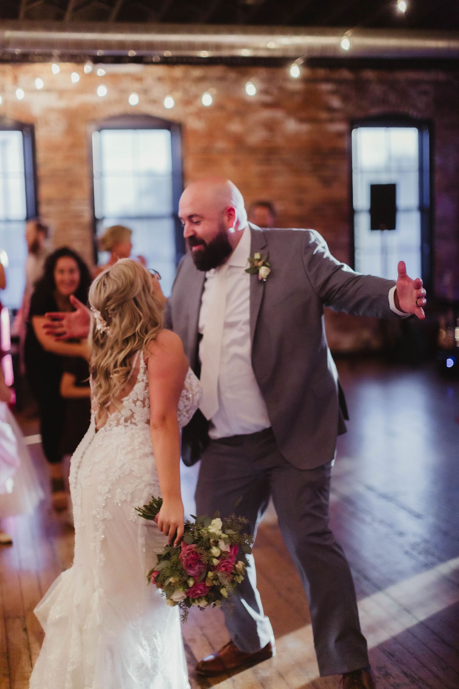 Couple dancing together at wedding reception in rustic brick venue with string lighting.