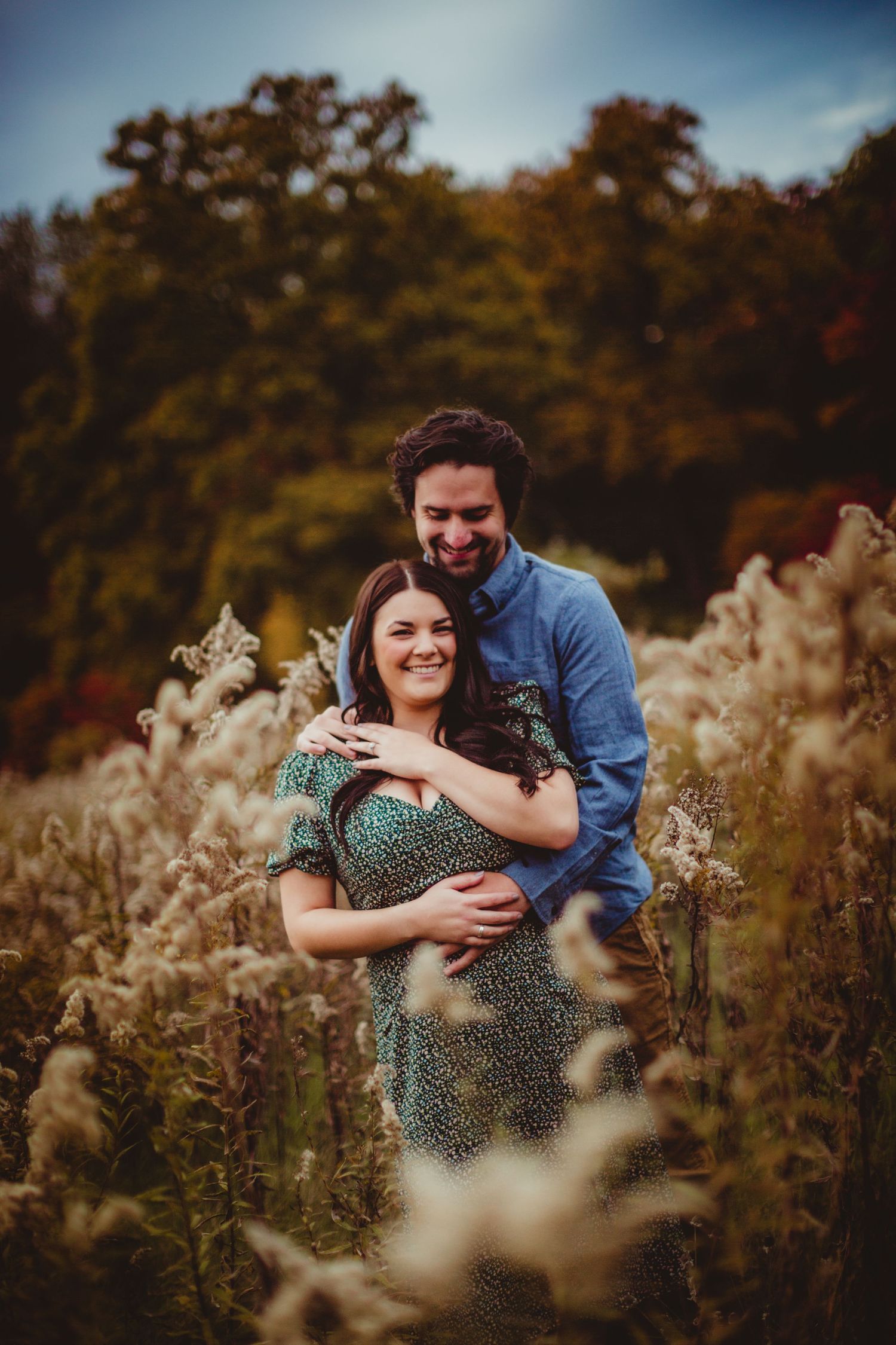 Tender embrace captured in natural fall setting with golden grass and trees.