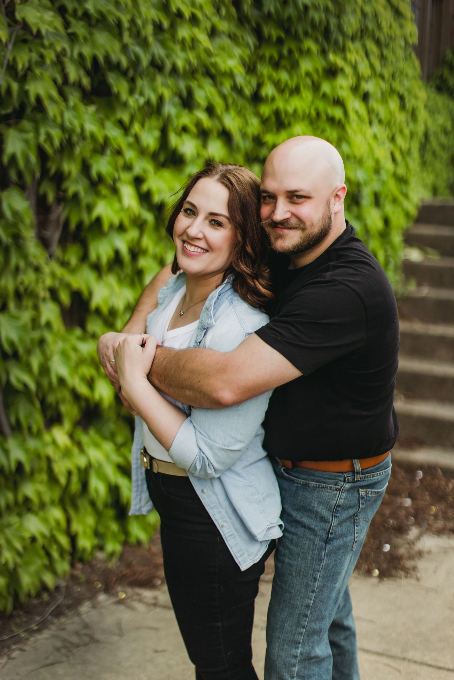 Loving embrace captured against lush green ivy covered wall.