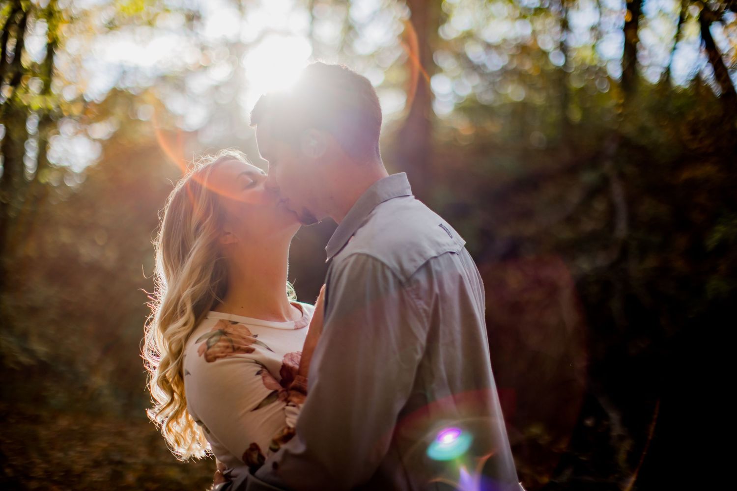 Intimate silhouetted portrait of couple embracing in sun-drenched autumn forest.