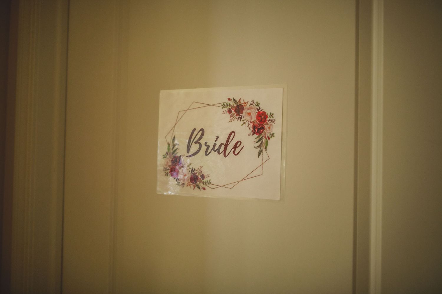 Wedding sign with floral design and 'Bride' text mounted on beige wall.