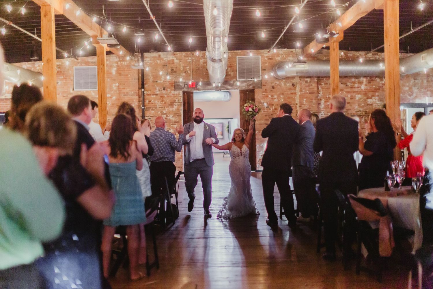 Dance floor at wedding reception with string lights and brick walls.