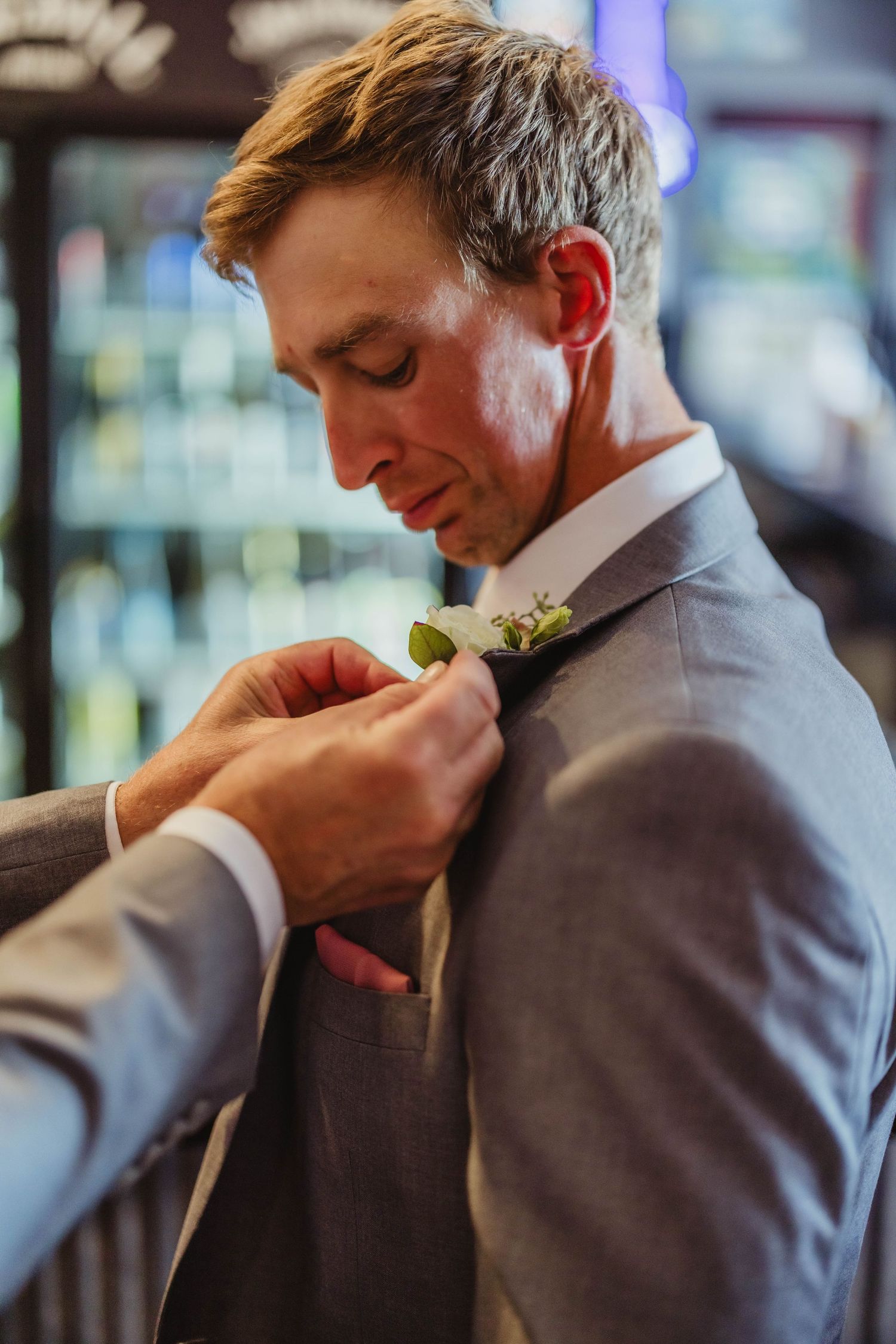 A boutonniere is carefully being adjusted on a grey suit jacket during wedding preparations.