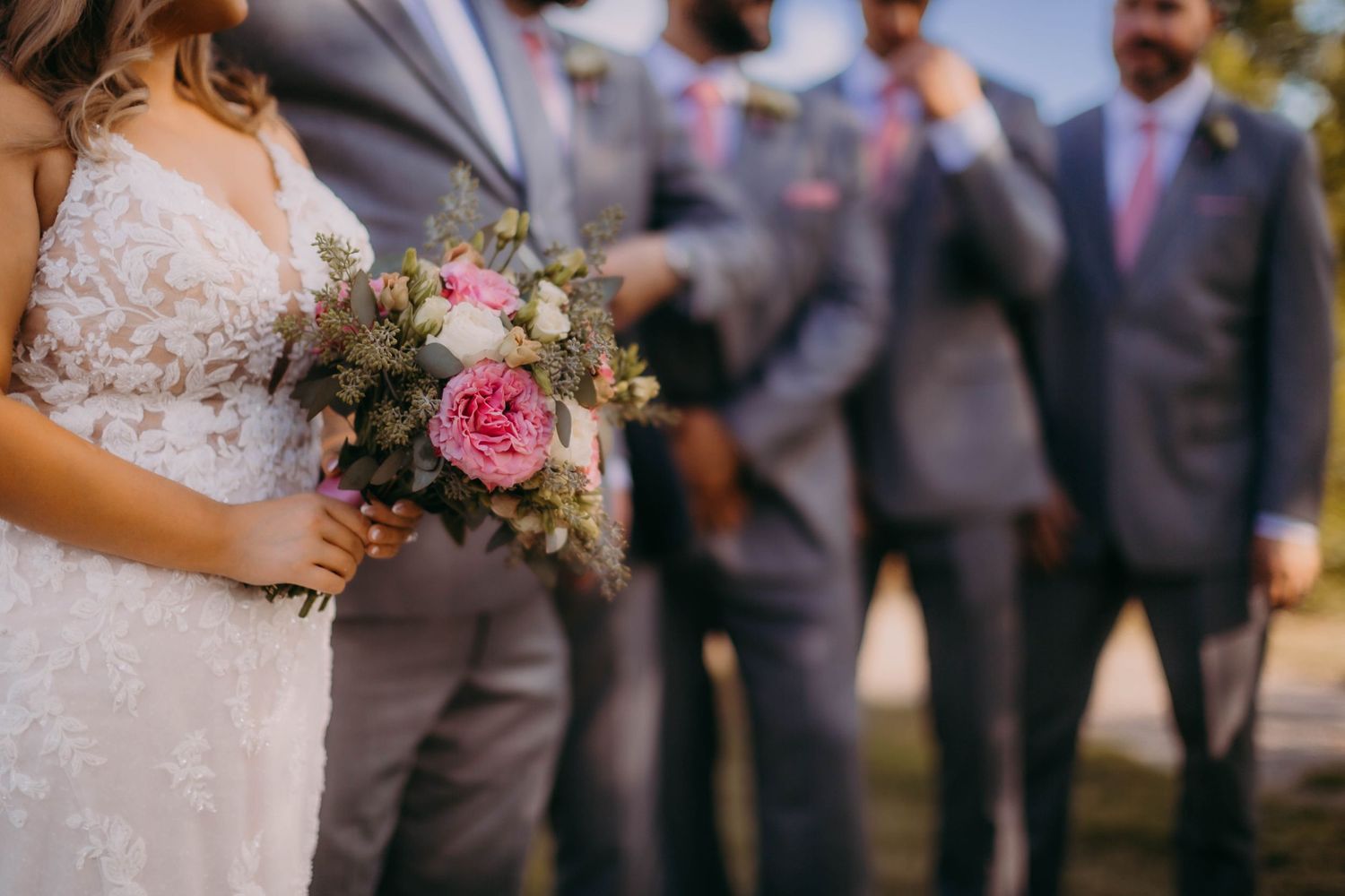 A wedding party stands together while the bride holds a beautiful pink and white bouquet.