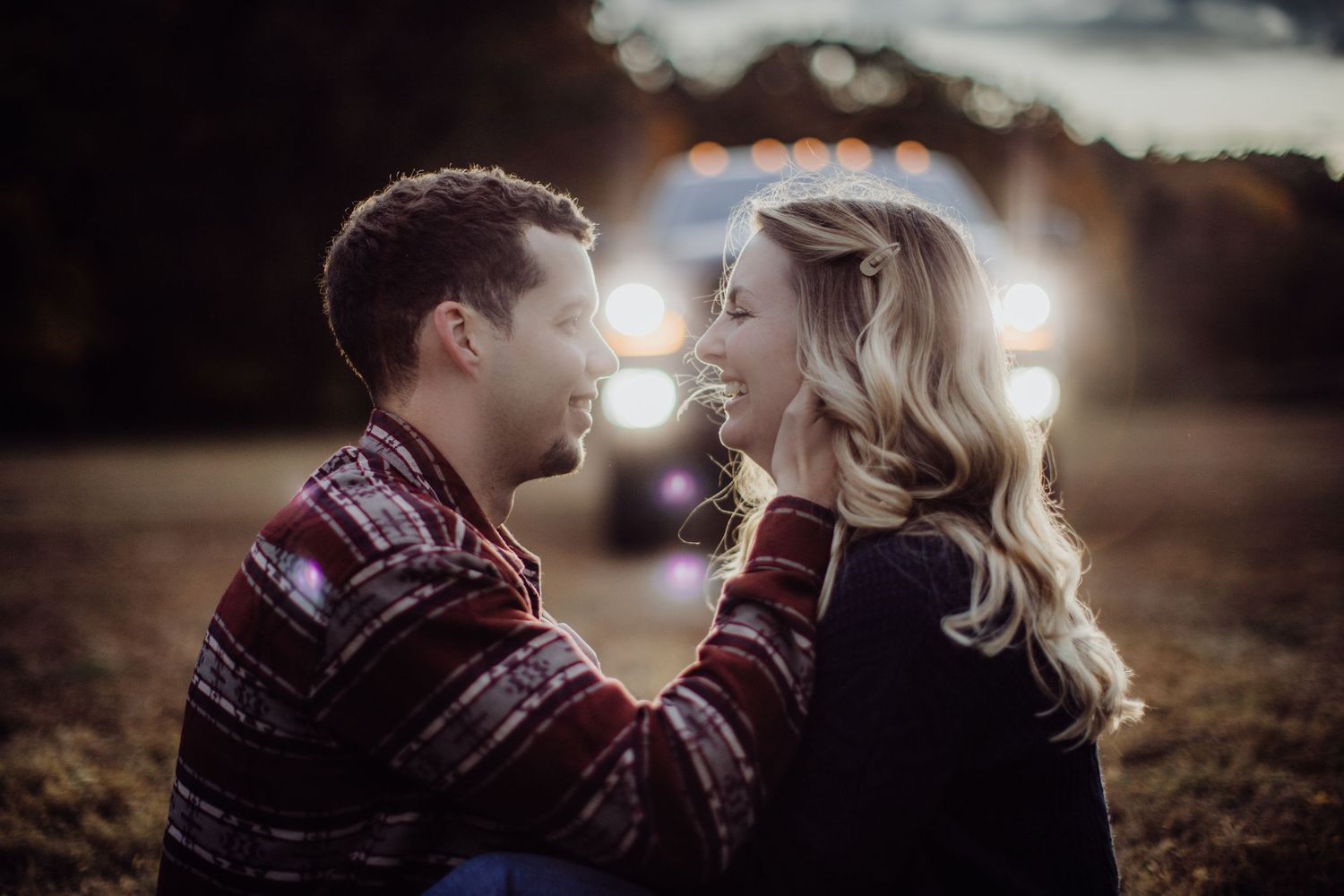 An intimate outdoor portrait with warm backlighting from vehicle headlights creating a romantic mood.