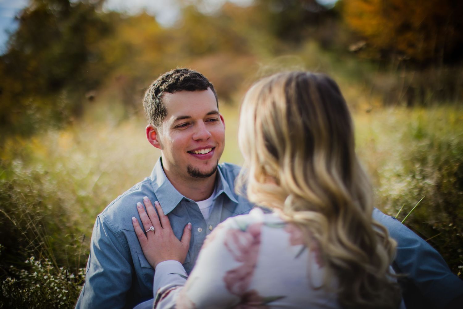 Intimate portrait of a couple in casual attire looking at each other in a sunlit autumn field.