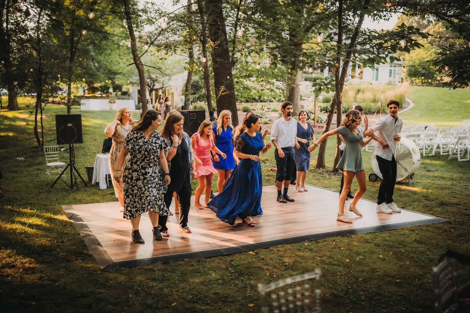 Wedding guests dancing on an outdoor wooden dance floor surrounded by trees.