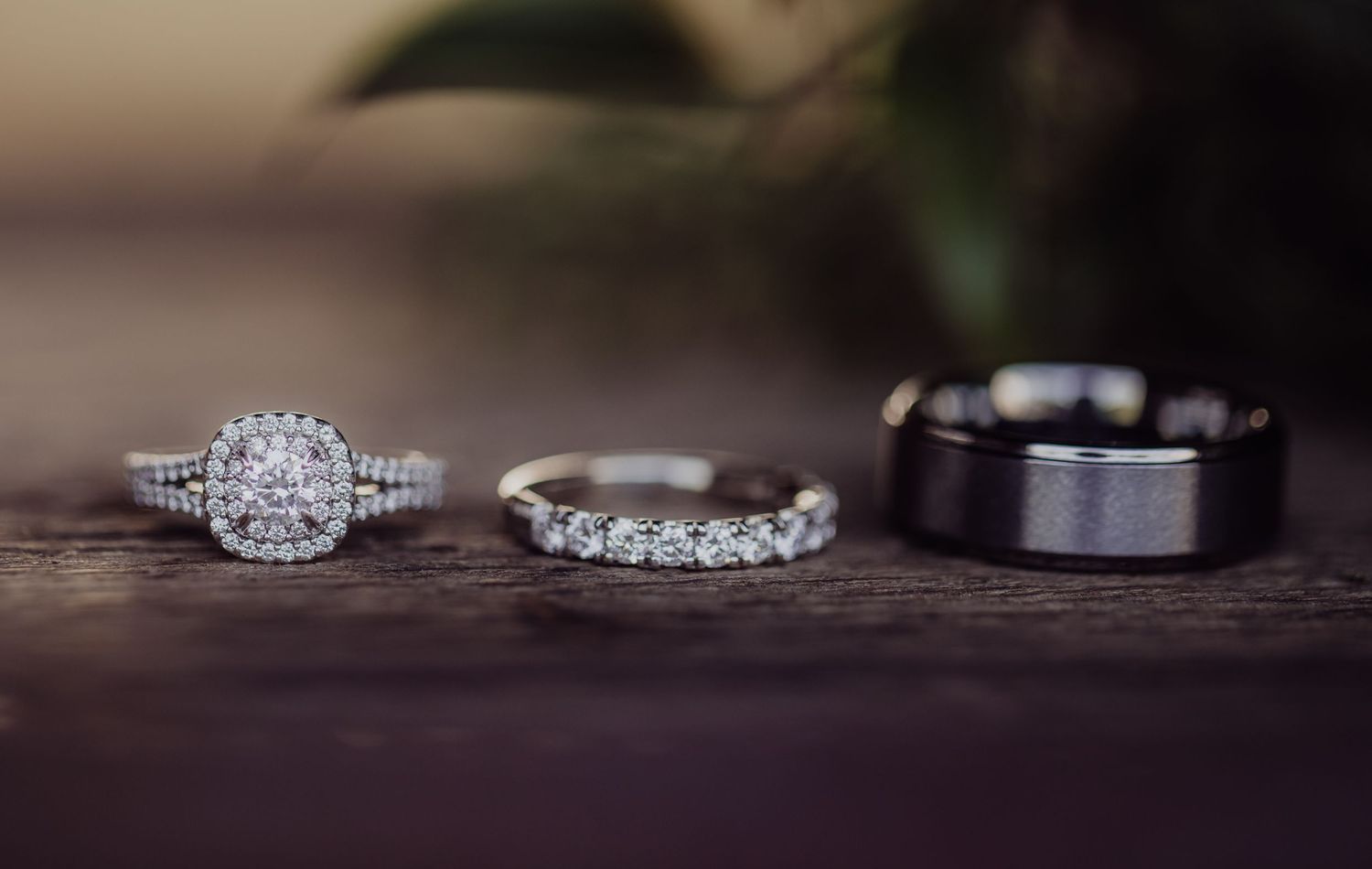 Wedding rings and sparkly diamond engagement ring displayed on dark surface with selective focus.
