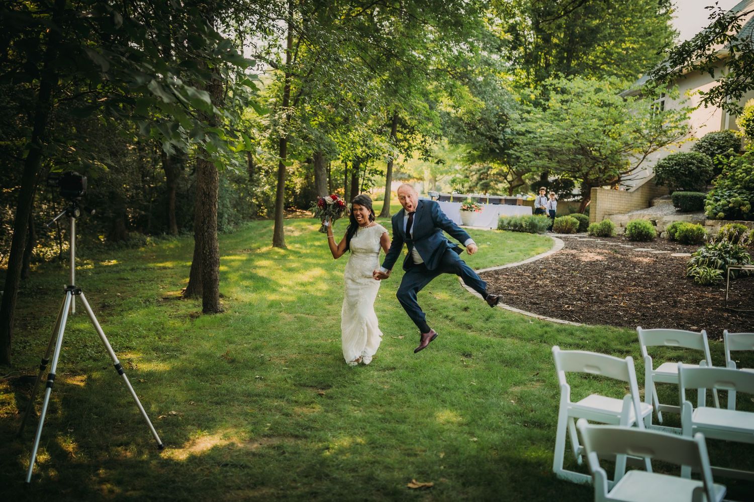 Wedding couple leaps joyfully down the outdoor ceremony aisle.