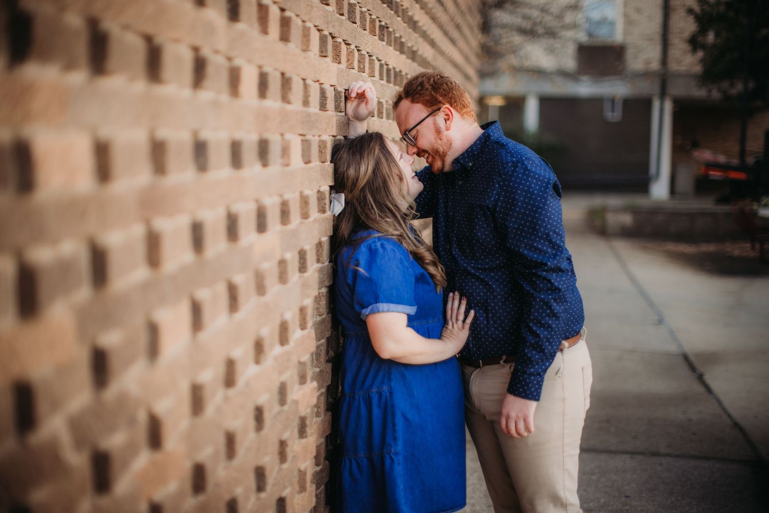 A couple embraces against a textured brick wall in an urban setting.
