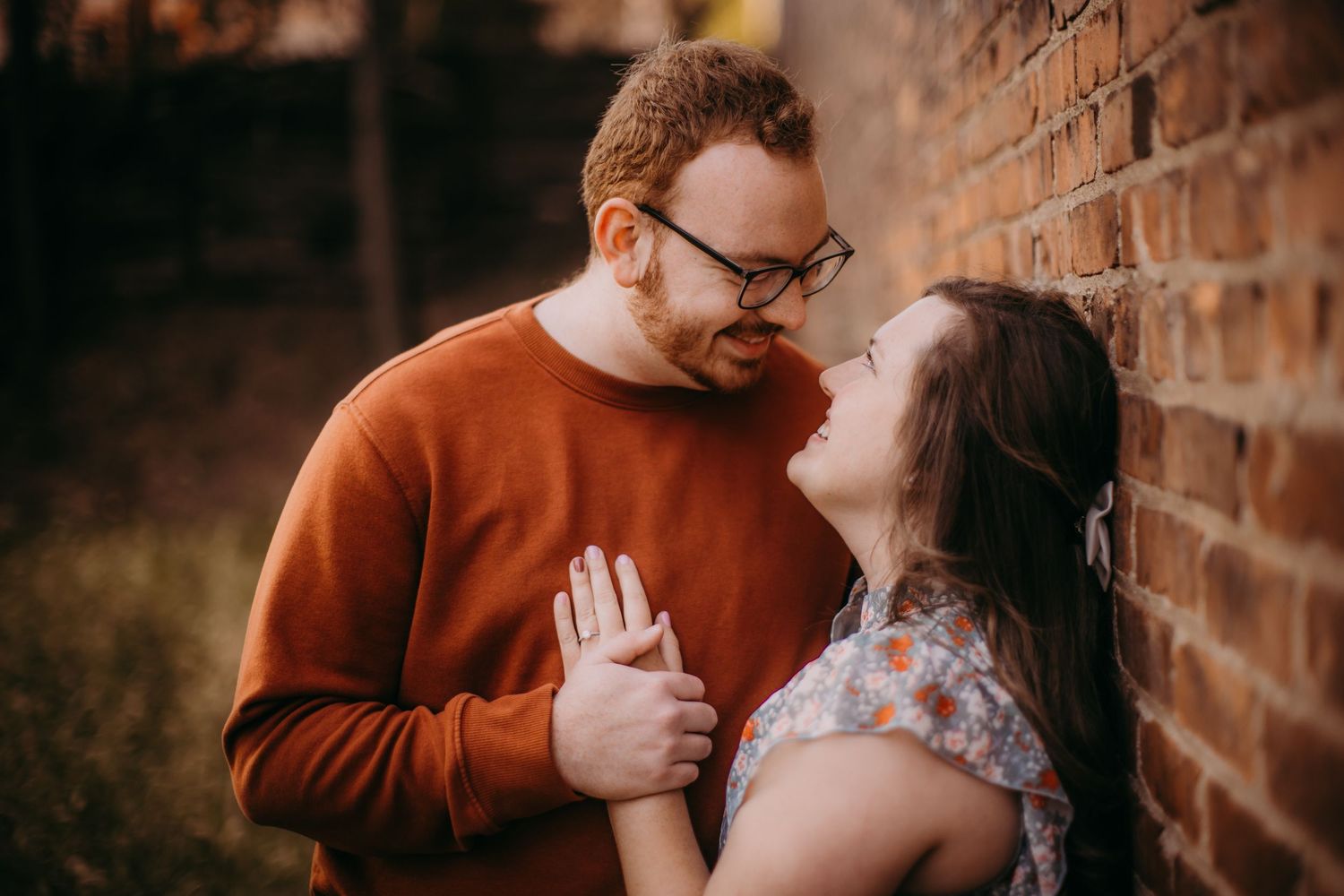 Candid engagement photography captures authentic emotions against historic brick walls.