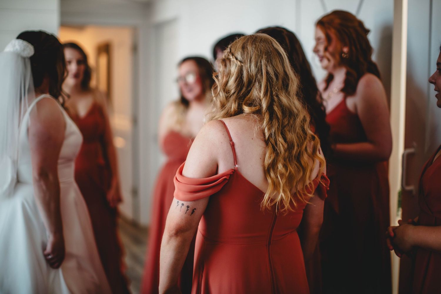 Row of bridesmaids in coral dresses stand together during wedding preparations.