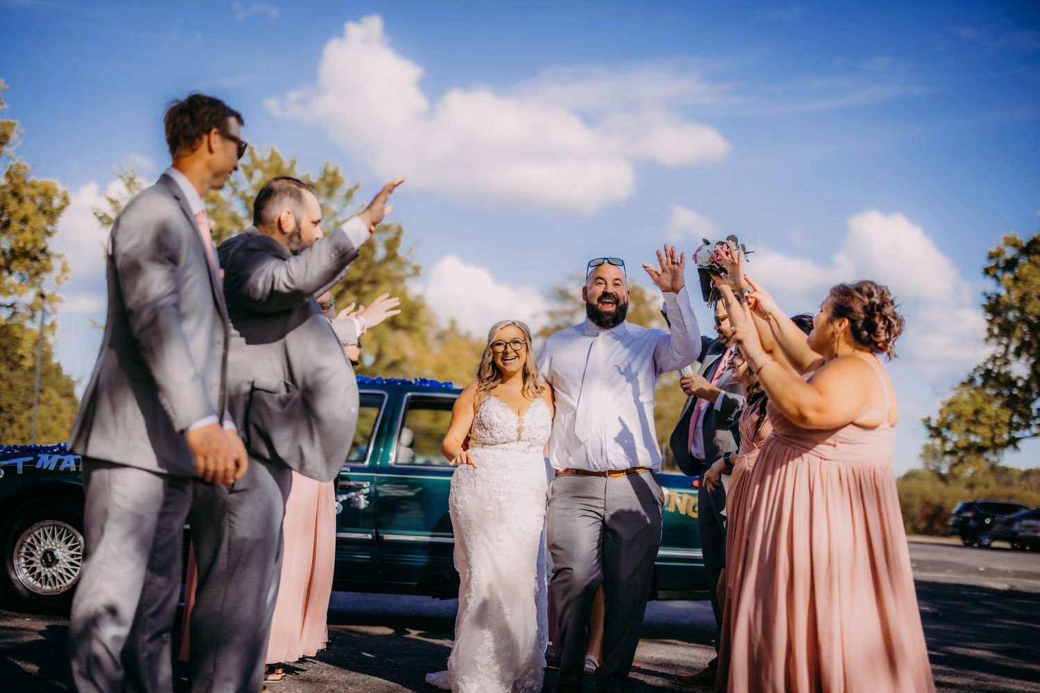 Joyful wedding party celebration with vintage car and coordinated pink and gray attire.