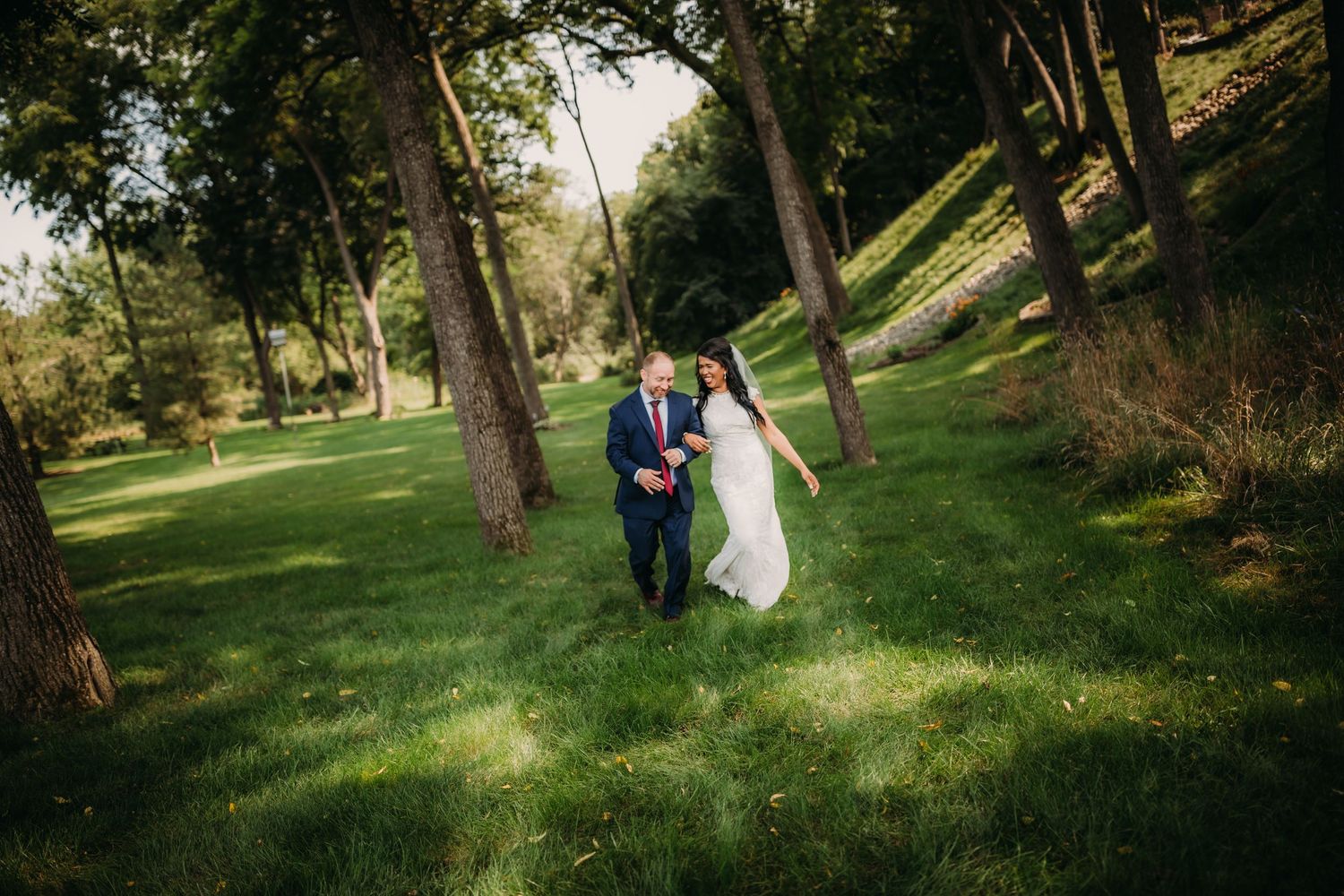 A wedding couple walks hand in hand through a serene wooded park.