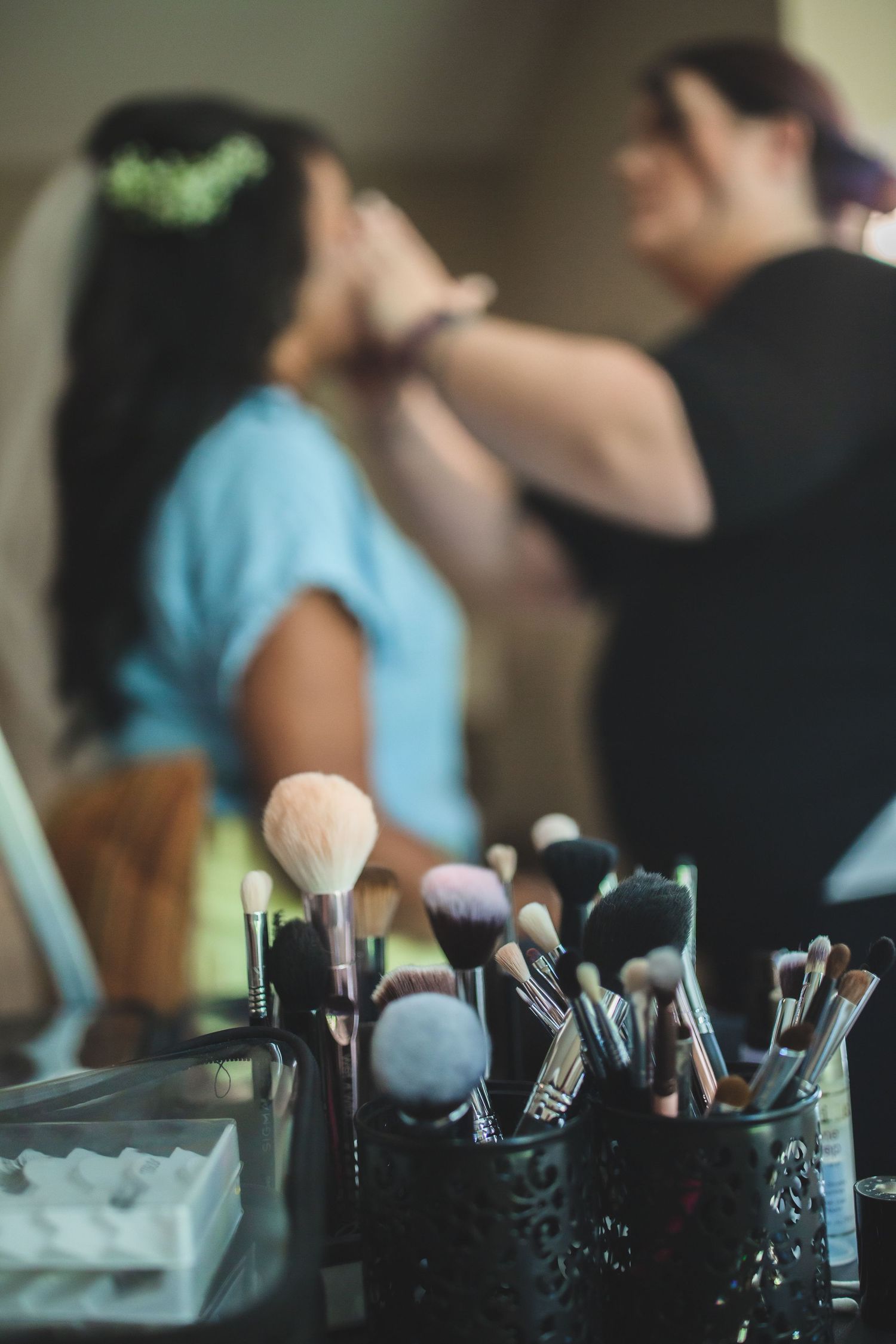 Professional makeup brushes arranged while stylist works with bride in background.
