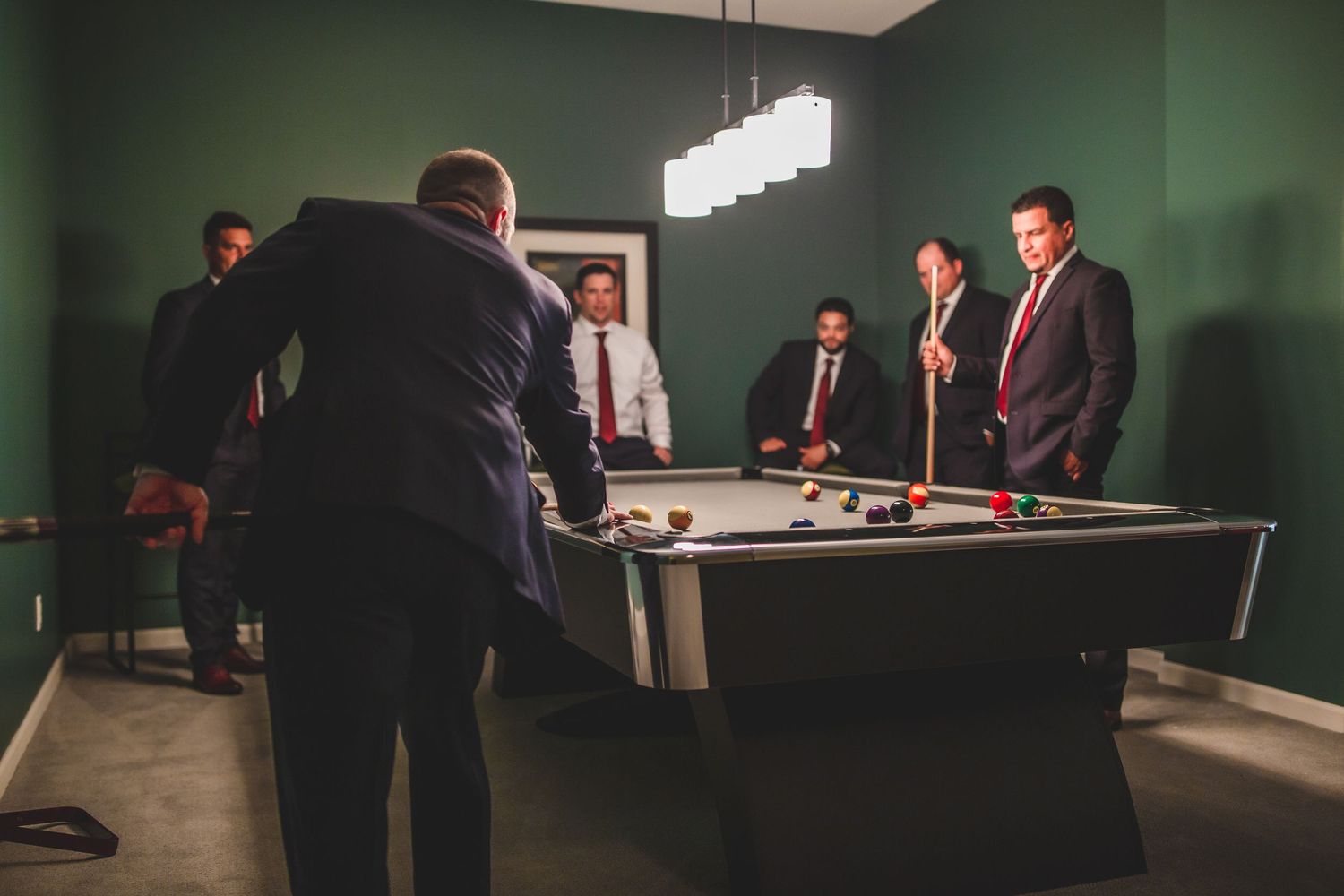 Several people in business attire gathered around a pool table under modern pendant lighting.