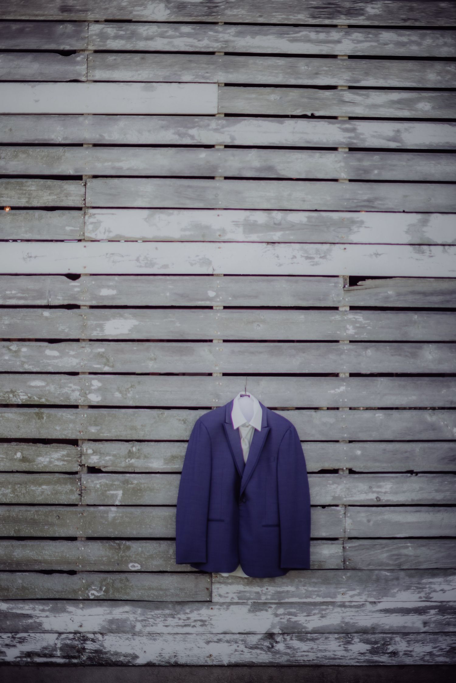 Navy blue suit jacket displayed against weathered white wooden wall background.