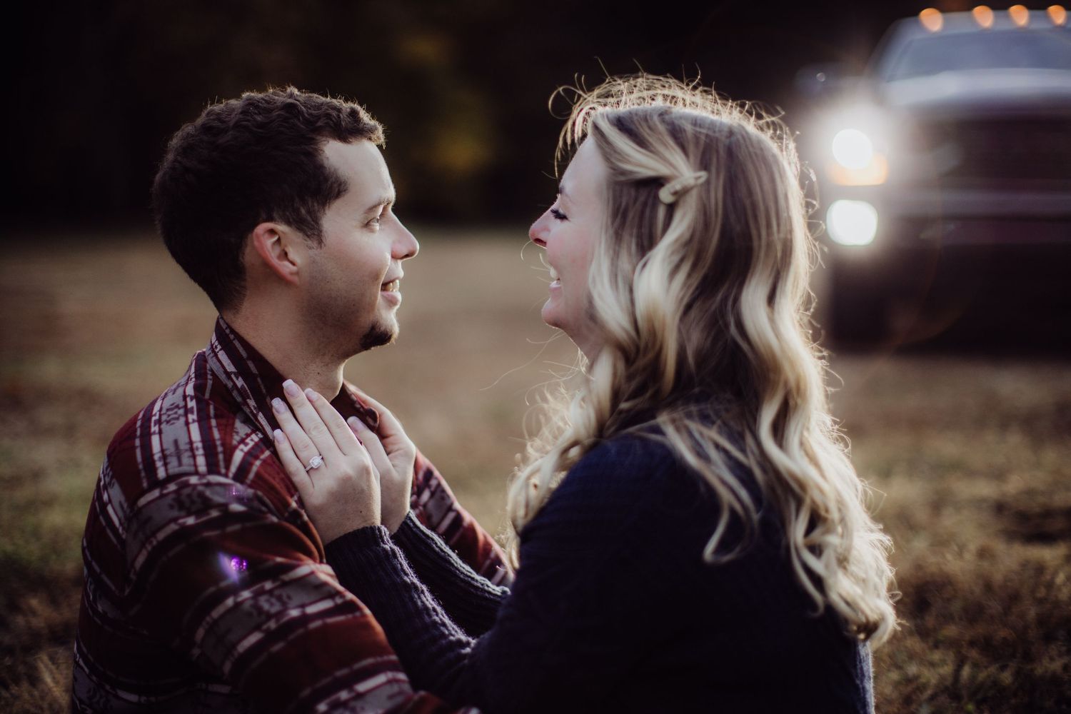 A tender embrace photographed outdoors with dramatic backlighting from a vehicle's headlights.