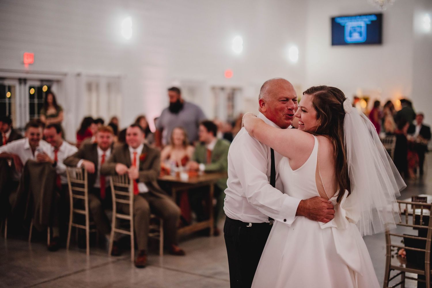 A couple embraces during their wedding dance while guests watch from decorated reception tables.