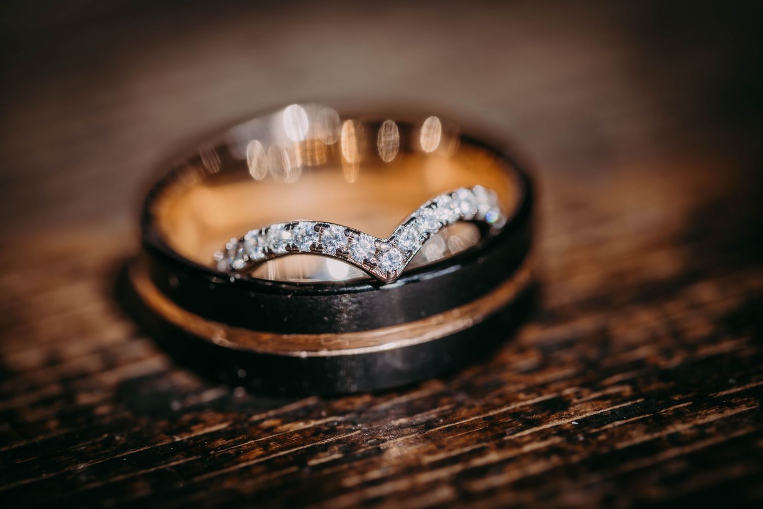 Wedding rings arranged on dark wooden surface with dramatic lighting.