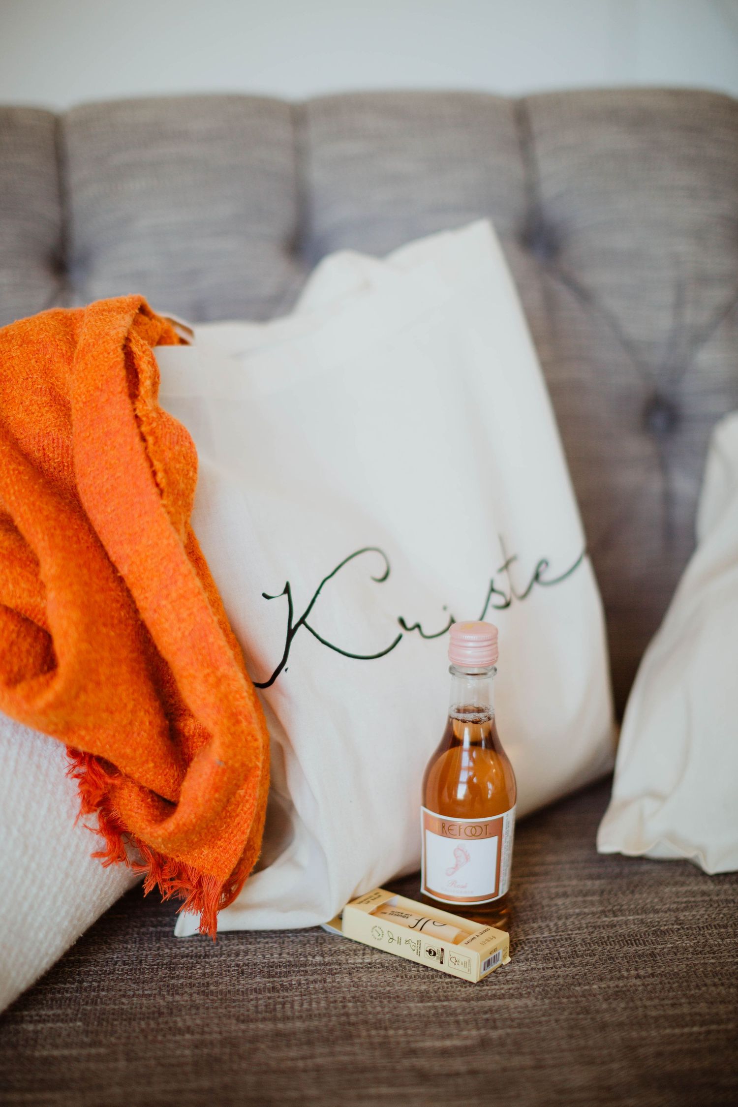 White linens with orange accents and small bottles arranged on a textured gray surface.