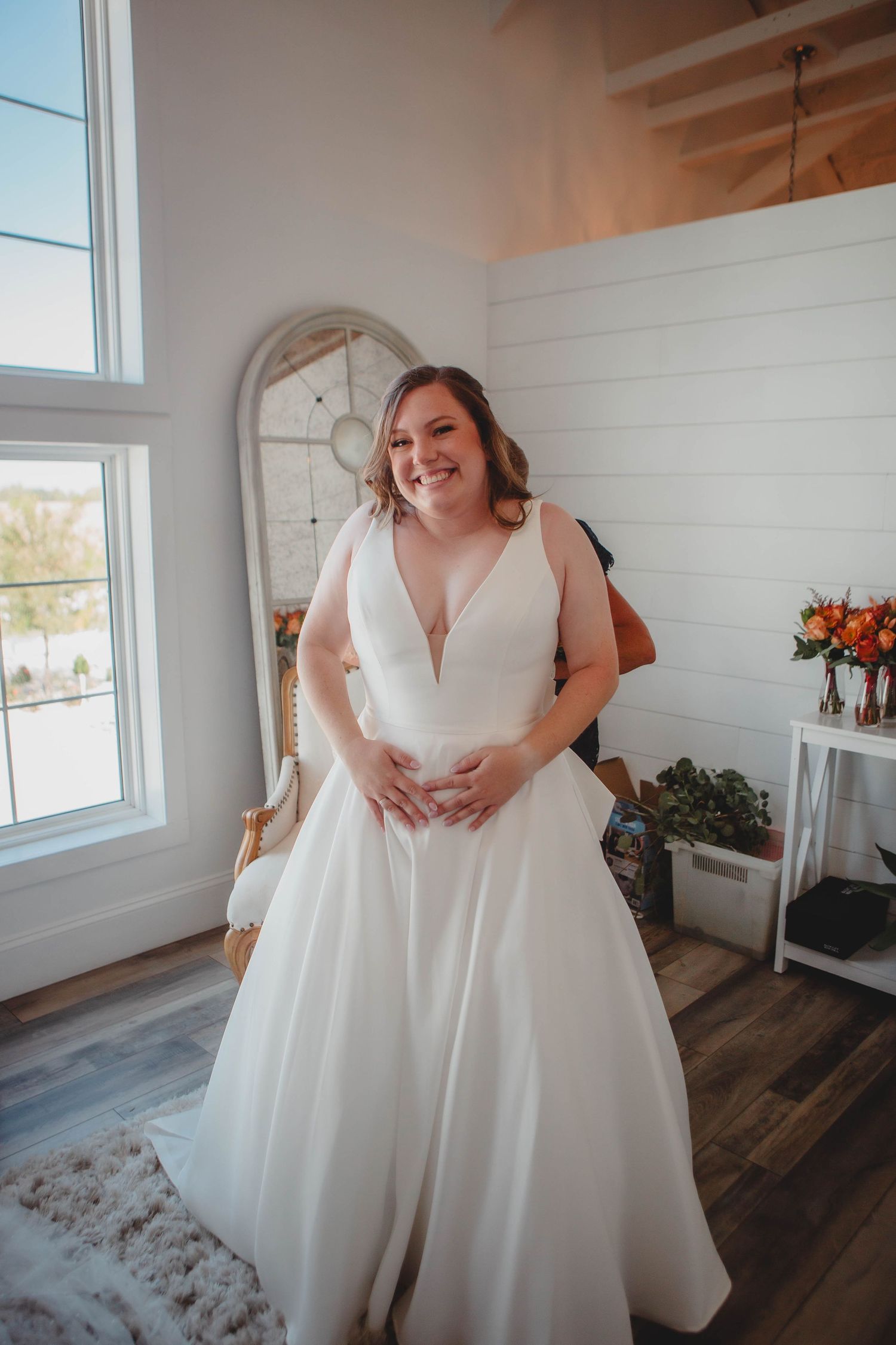 Two people in white wedding dresses sharing a joyful moment in a sun-lit room.
