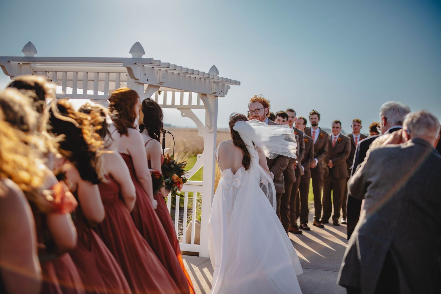 Wedding party lined up during outdoor ceremony with bridesmaids in burgundy dresses.