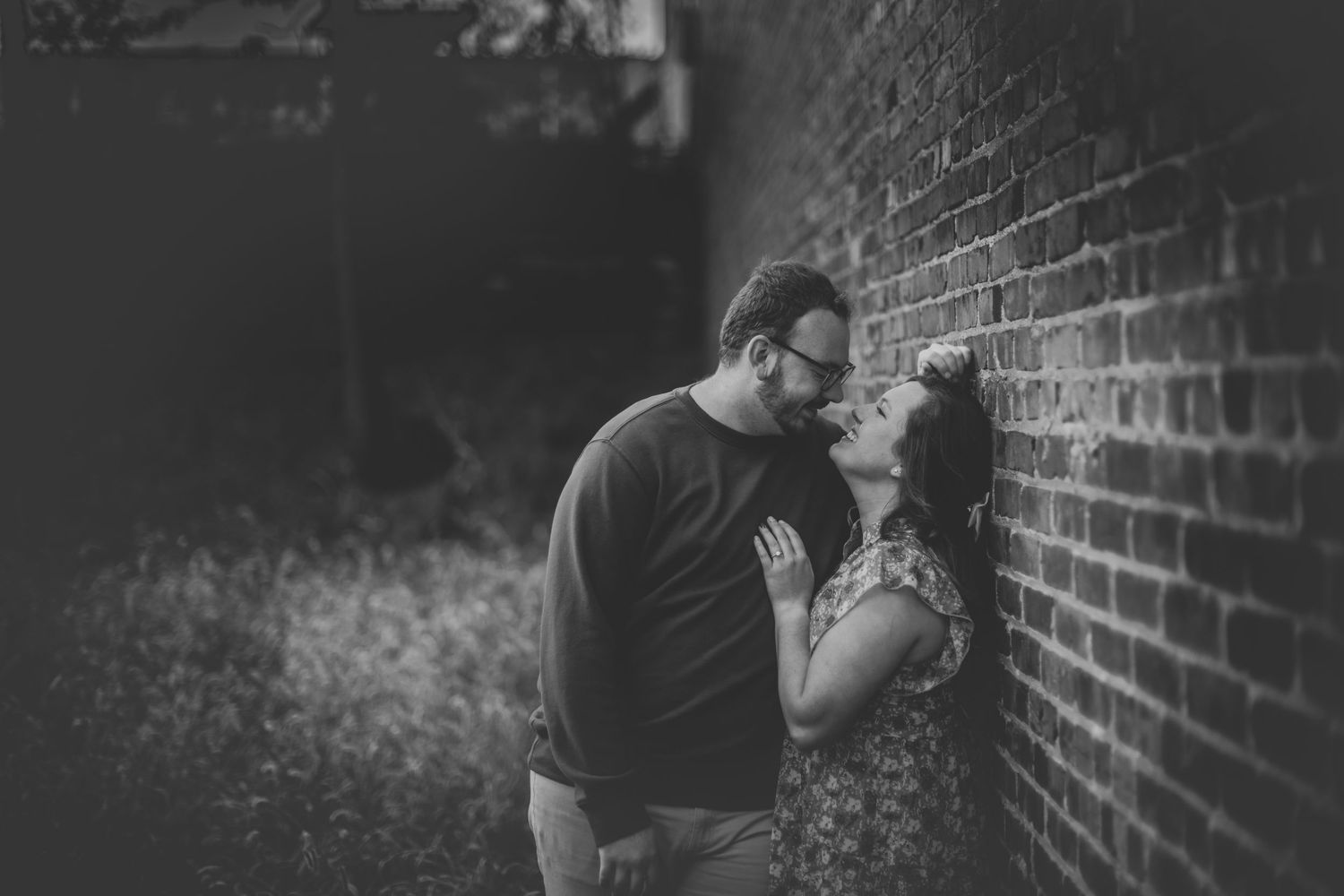 Black and white portrait of a couple sharing tender moments against an urban brick backdrop.