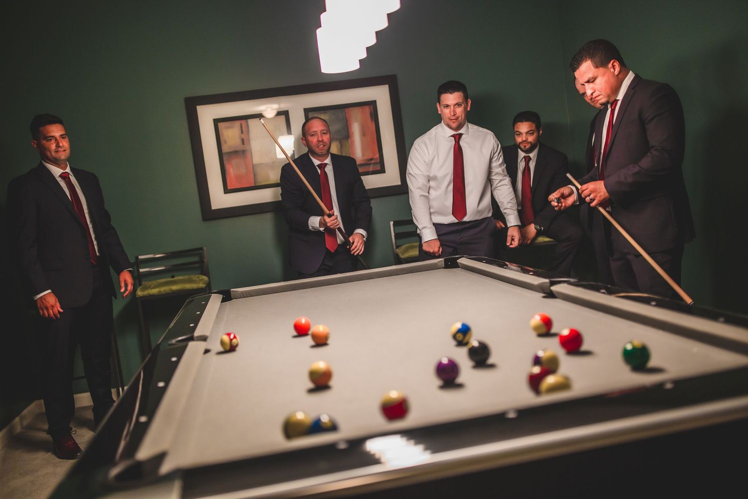 Men in suits and ties playing billiards on a pool table in a room with dark green walls.