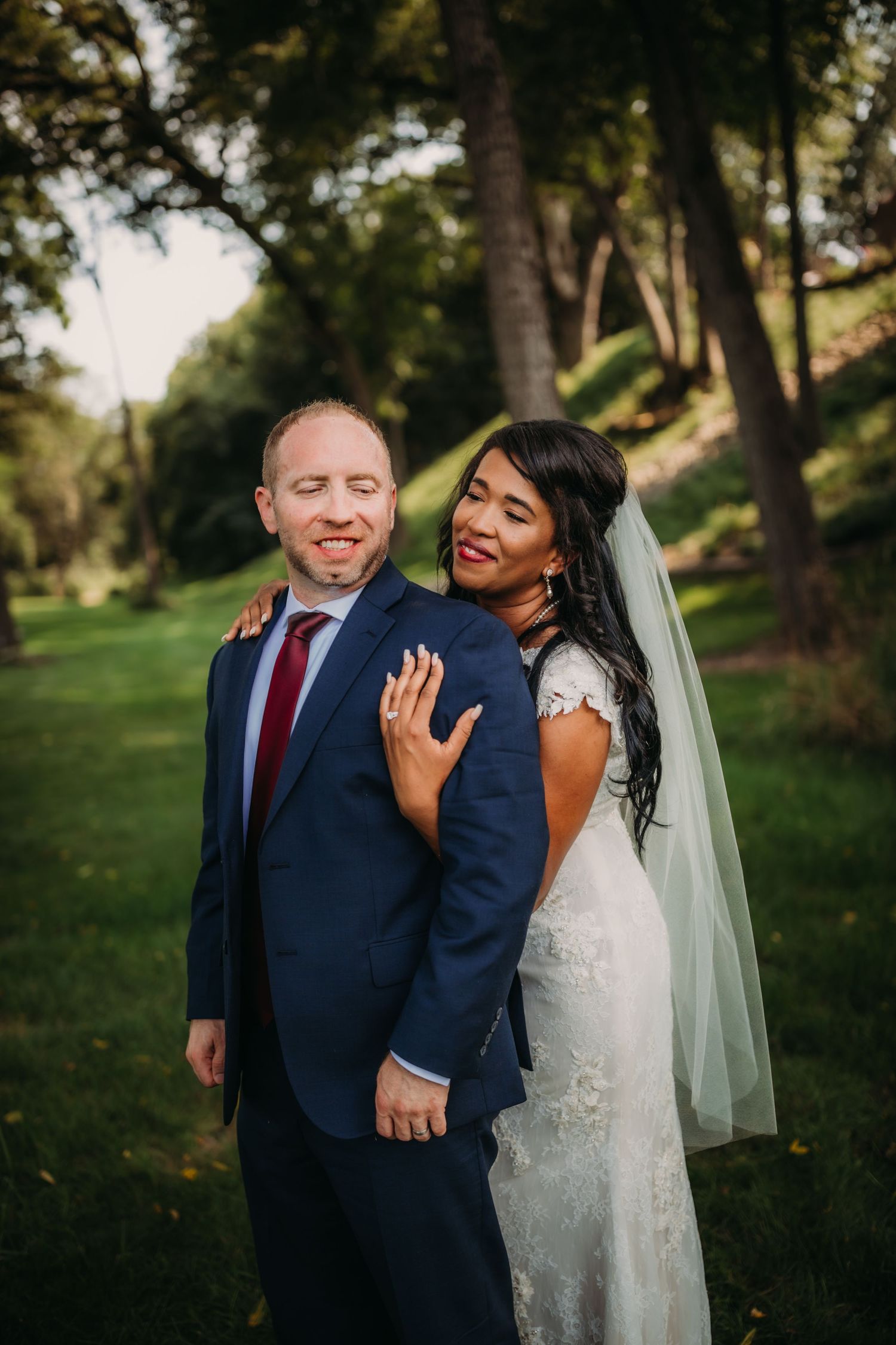 Newlyweds pose for a candid portrait in a sunlit garden setting.