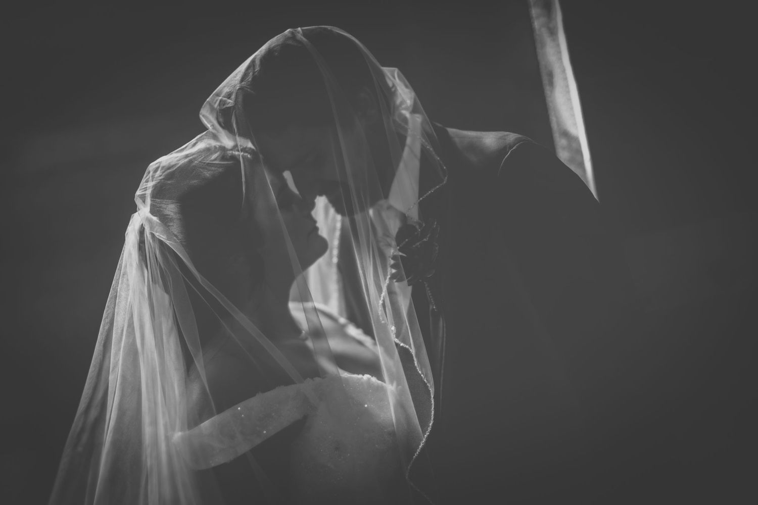 Black and white wedding portrait showing a tender moment beneath a flowing veil.
