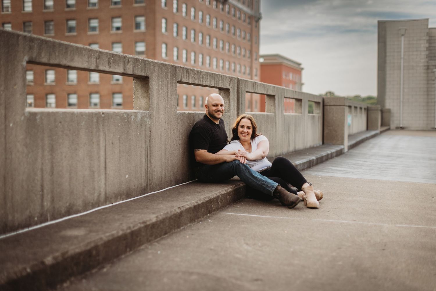 A couple shares an intimate moment while sitting on a concrete barrier in an urban setting.