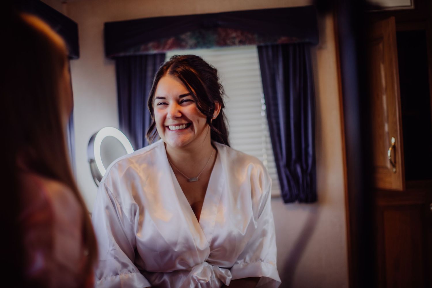 Someone wearing a white robe laughs joyfully while getting ready in a room with blue curtains.
