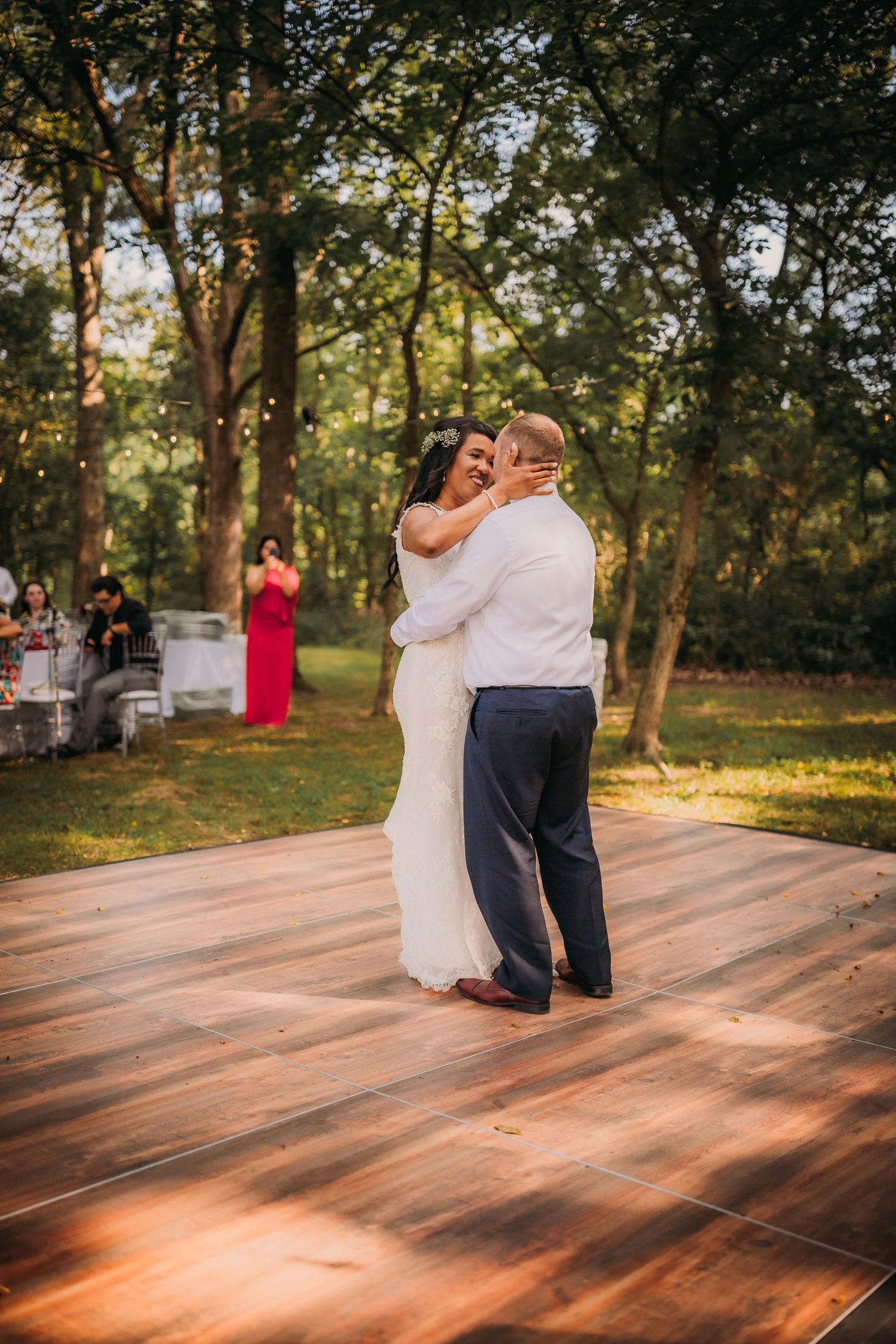 A couple embraces during their first dance on a rustic wooden dance floor surrounded by trees.