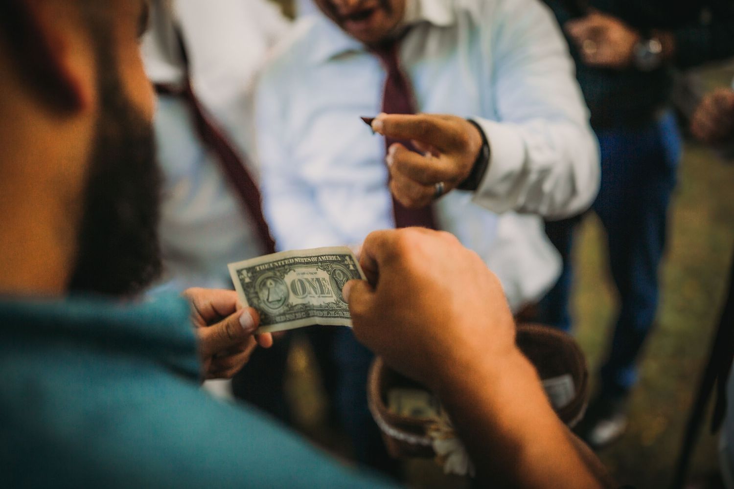 Hands exchanging dollar bills during an outdoor gathering.