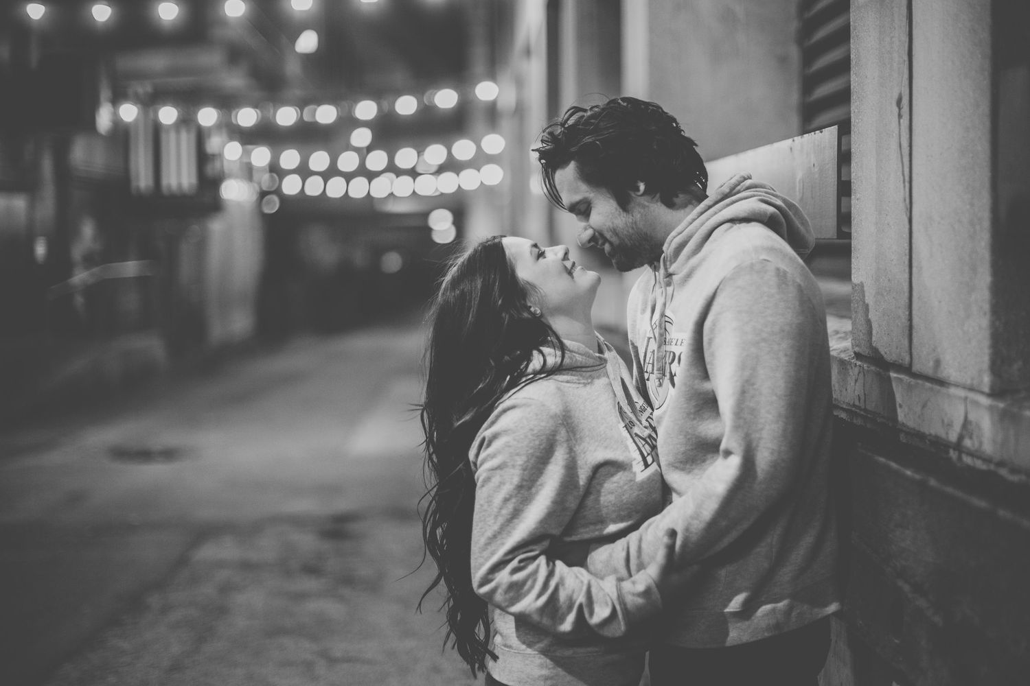 Romantic couple embraces under twinkling lights at night in an urban setting.