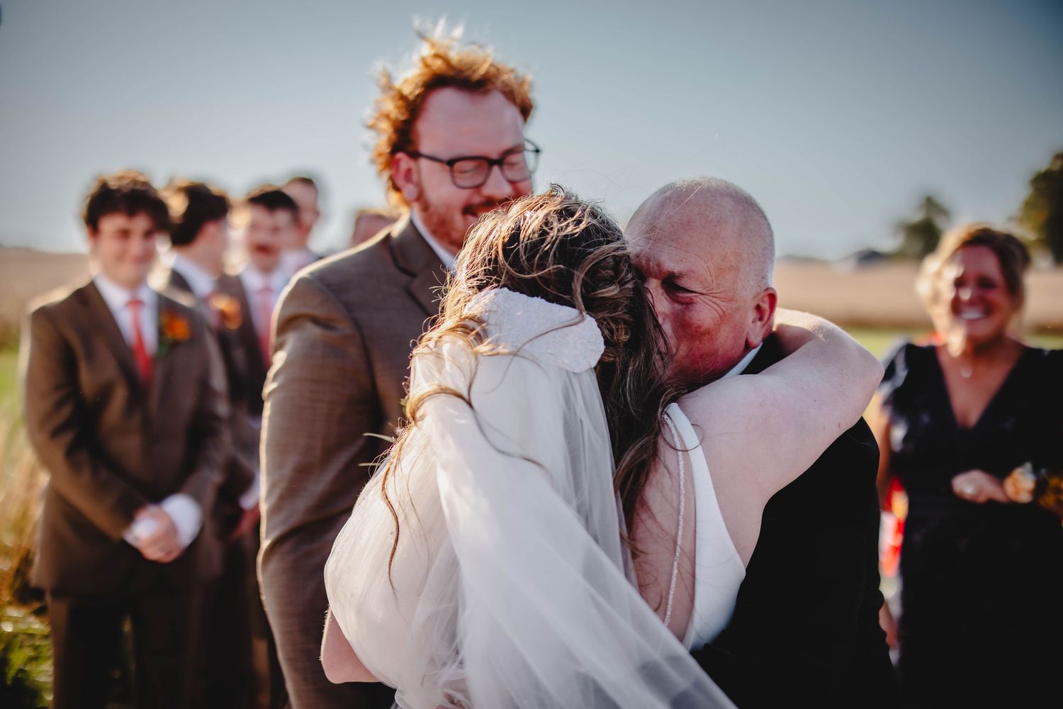 Tender emotional moment during outdoor wedding ceremony with guests looking on.