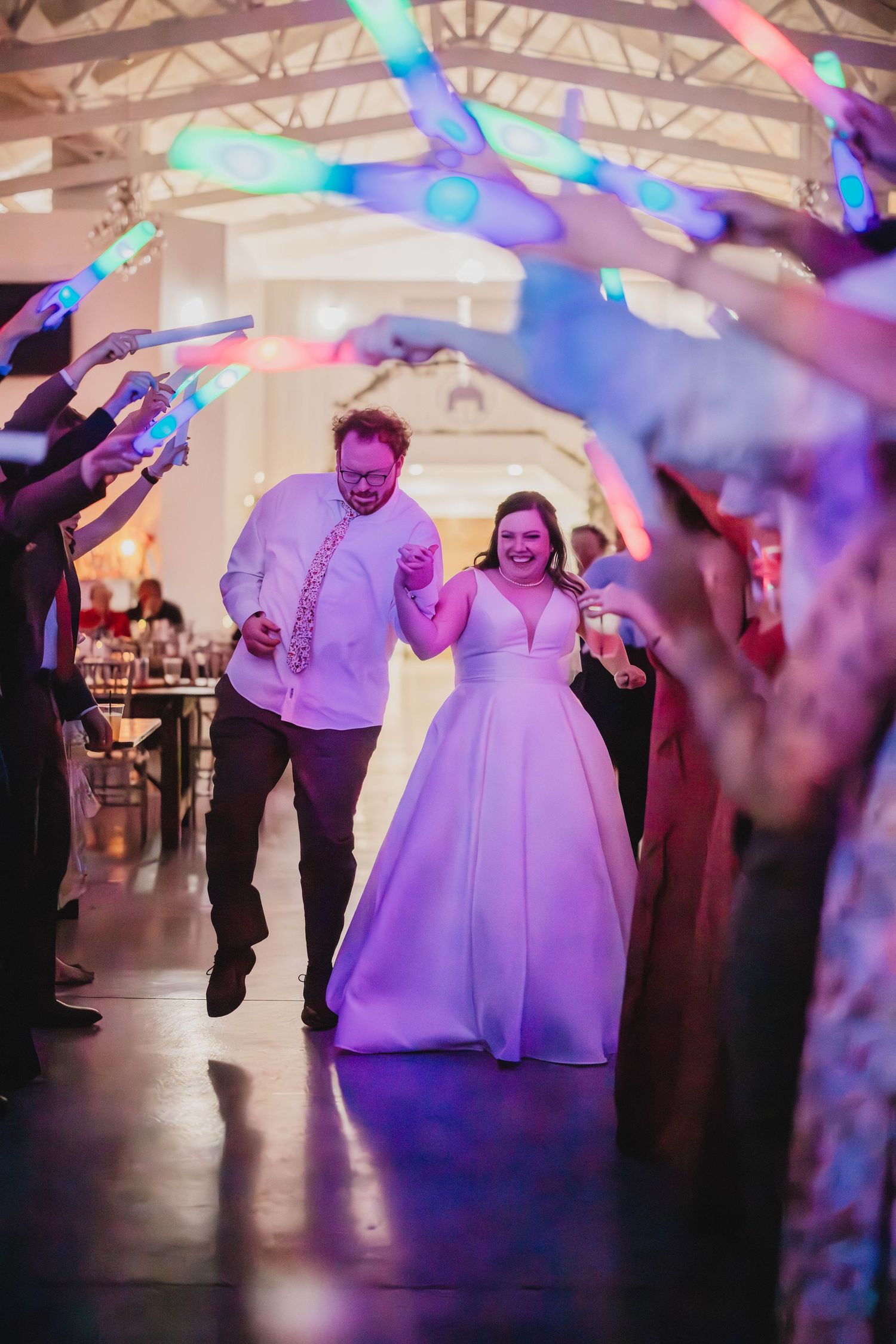 Couple makes grand entrance at wedding reception while guests wave light sticks forming a tunnel.
