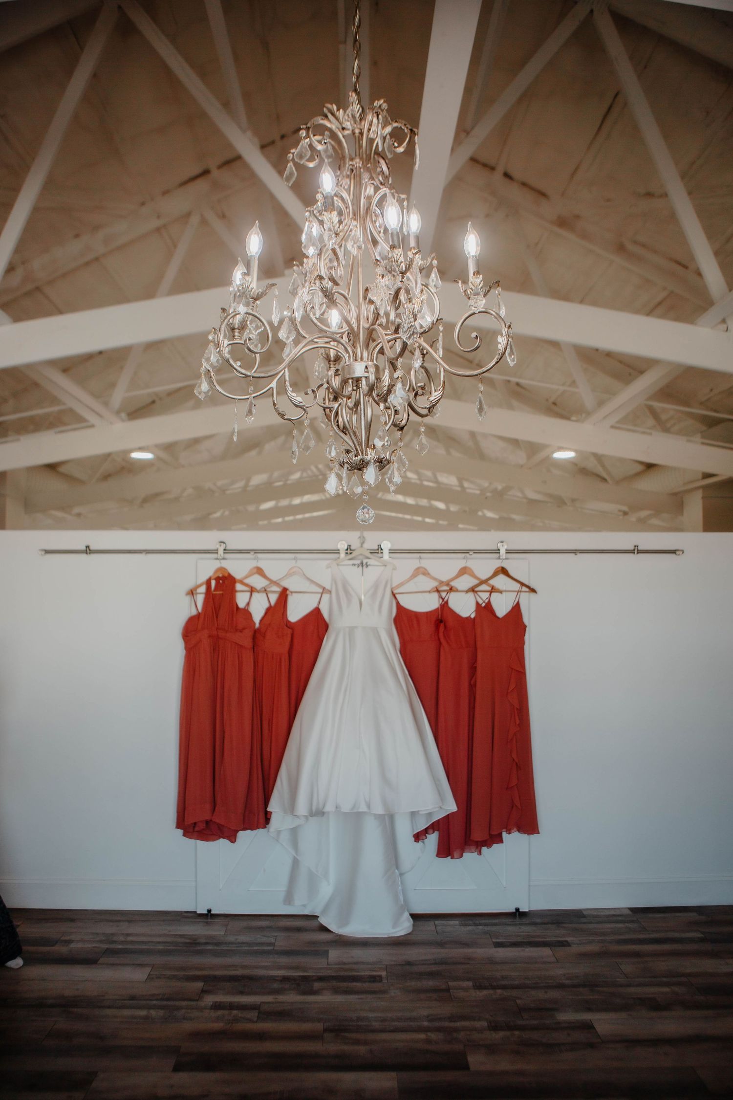 Crystal chandelier illuminates white wedding gown flanked by coral bridesmaid dresses.