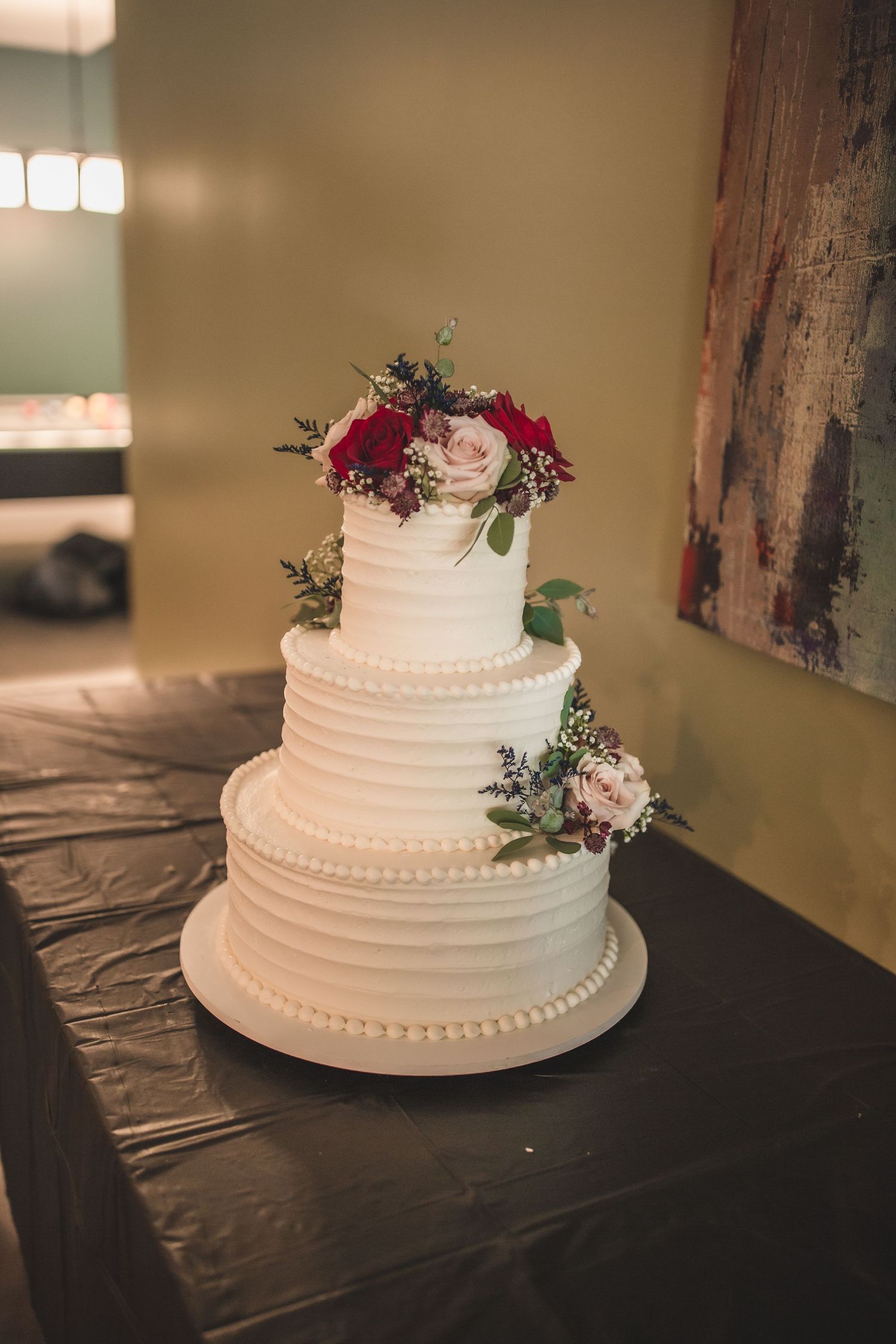 Classic three-tiered white wedding cake decorated with red and pink roses and greenery.