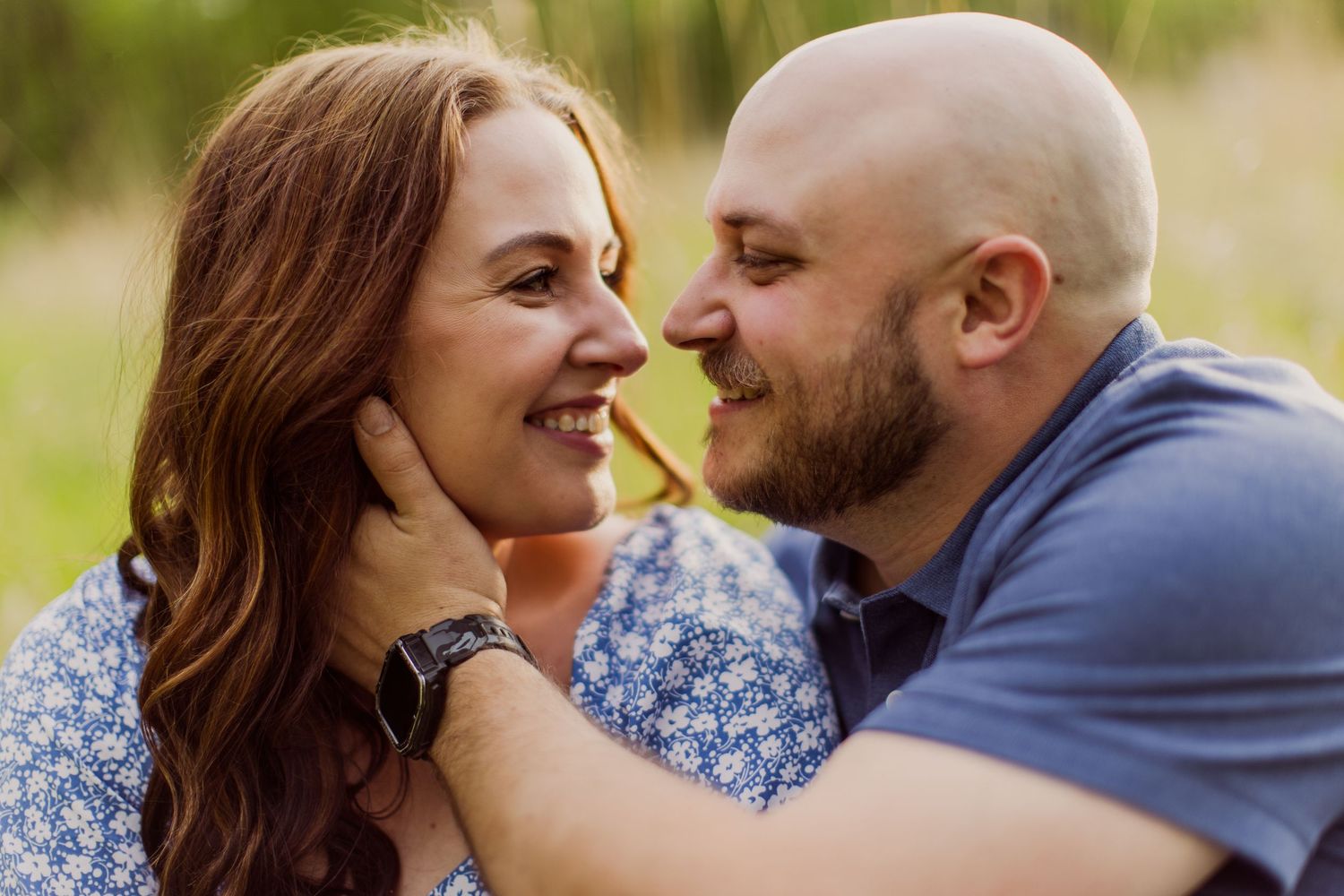 Romantic couple shares intimate moment while lying in grass during golden hour sunset photography session.