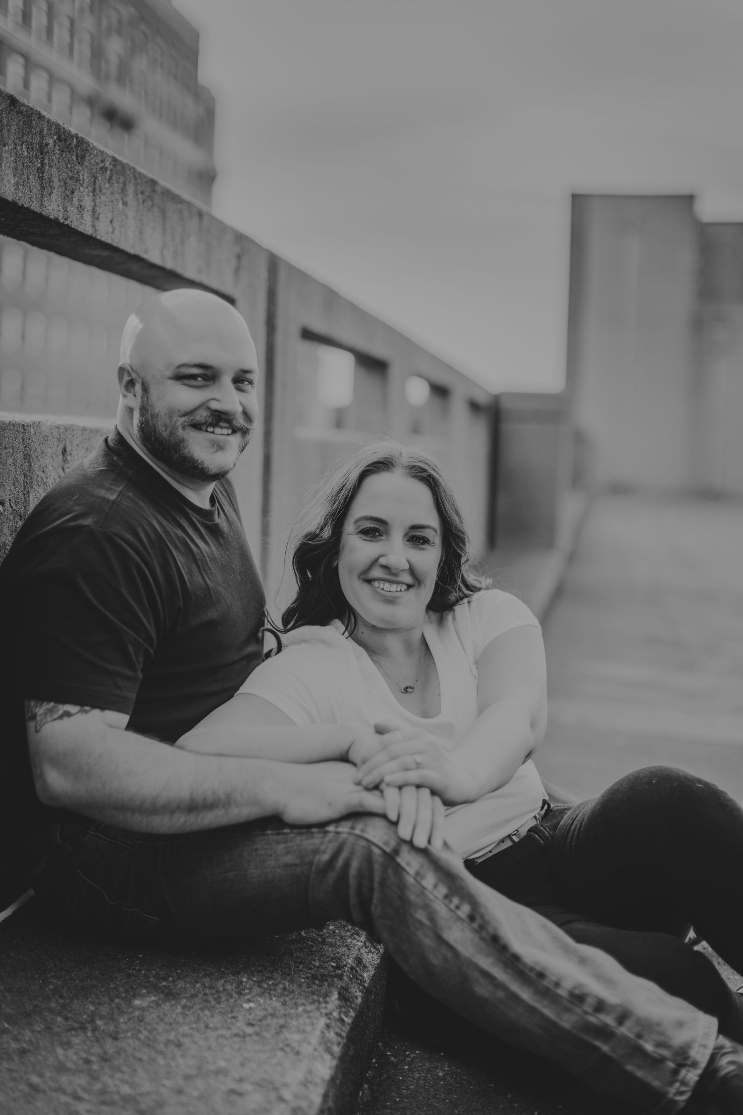 Black and white image of a couple relaxing and smiling in an urban setting.